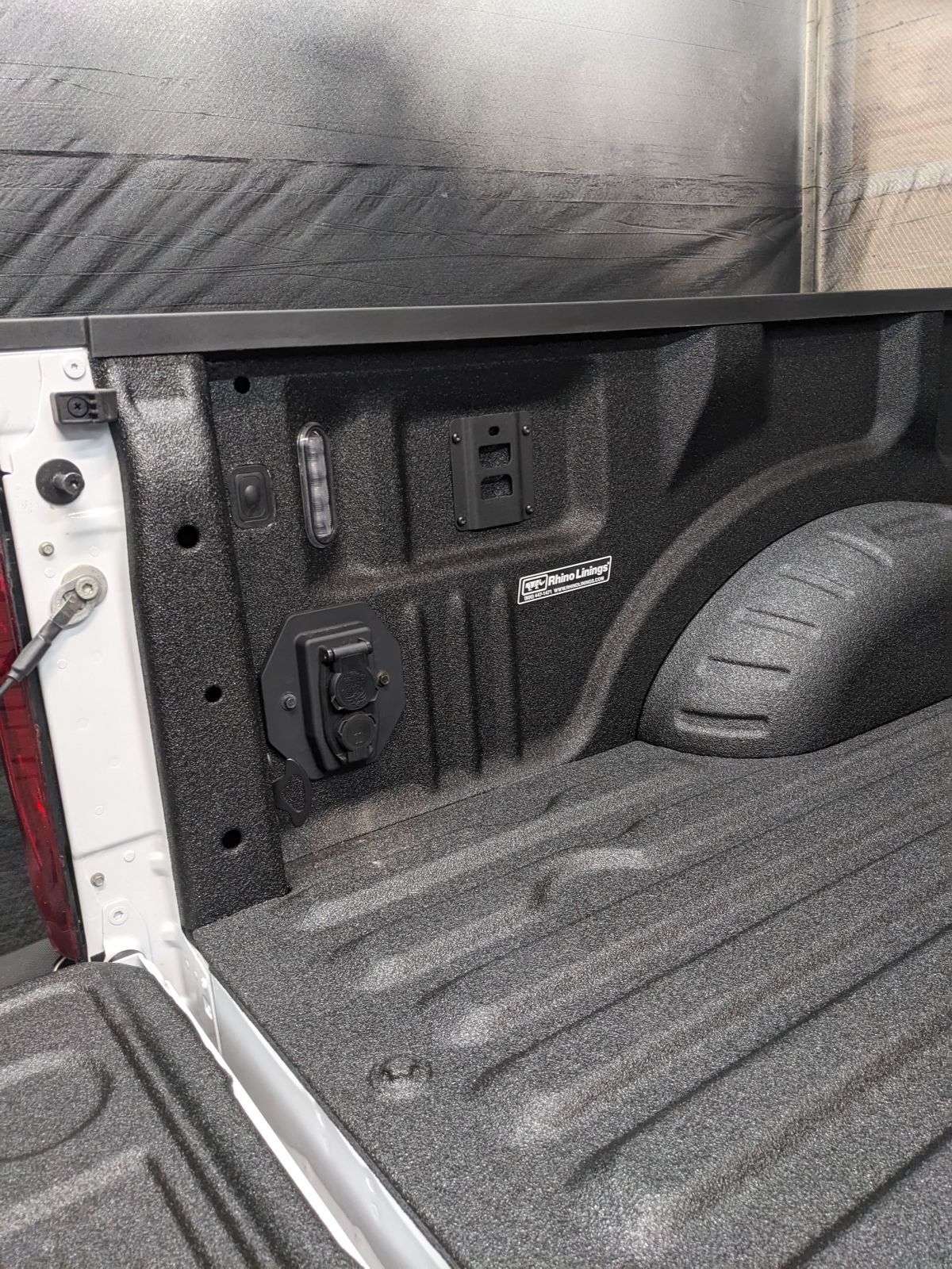 Truck bed with textured black liner, electrical outlets, and white exterior panel.