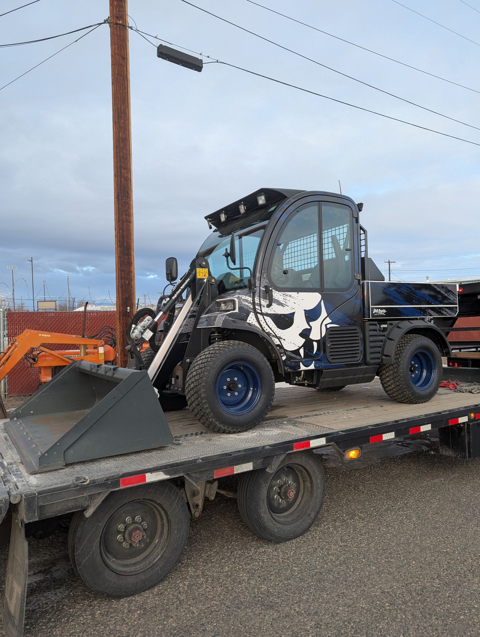 Black and blue utility vehicle with skull decals on a trailer, near utility poles.
