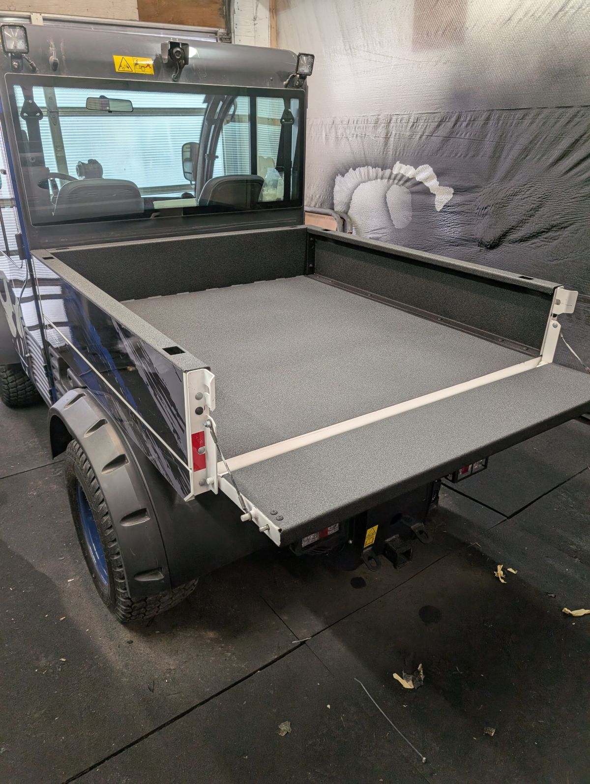 Utility vehicle with open bed, lowered tailgate, grey bed liner, and rear view.