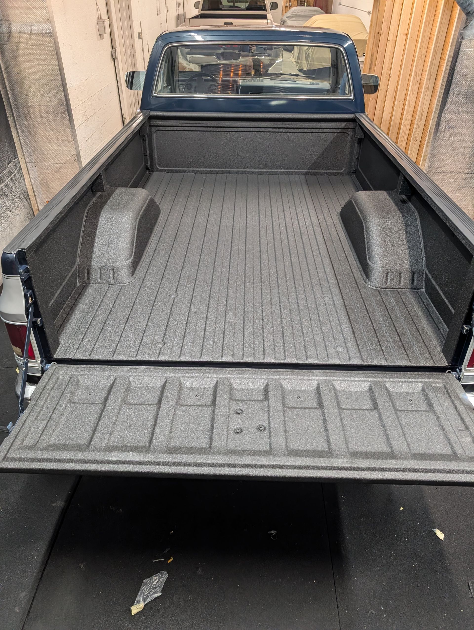 Open tailgate of a dark blue pickup truck bed with a textured gray coating.