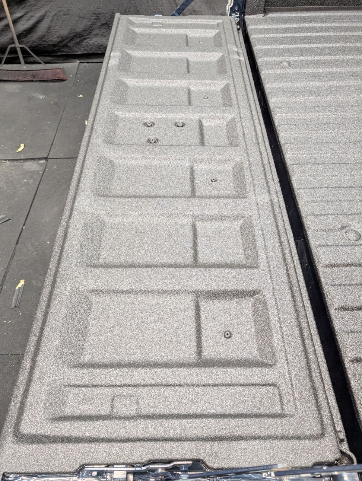 Gray truck bed cover with textured, raised panels and a small lock mechanism.