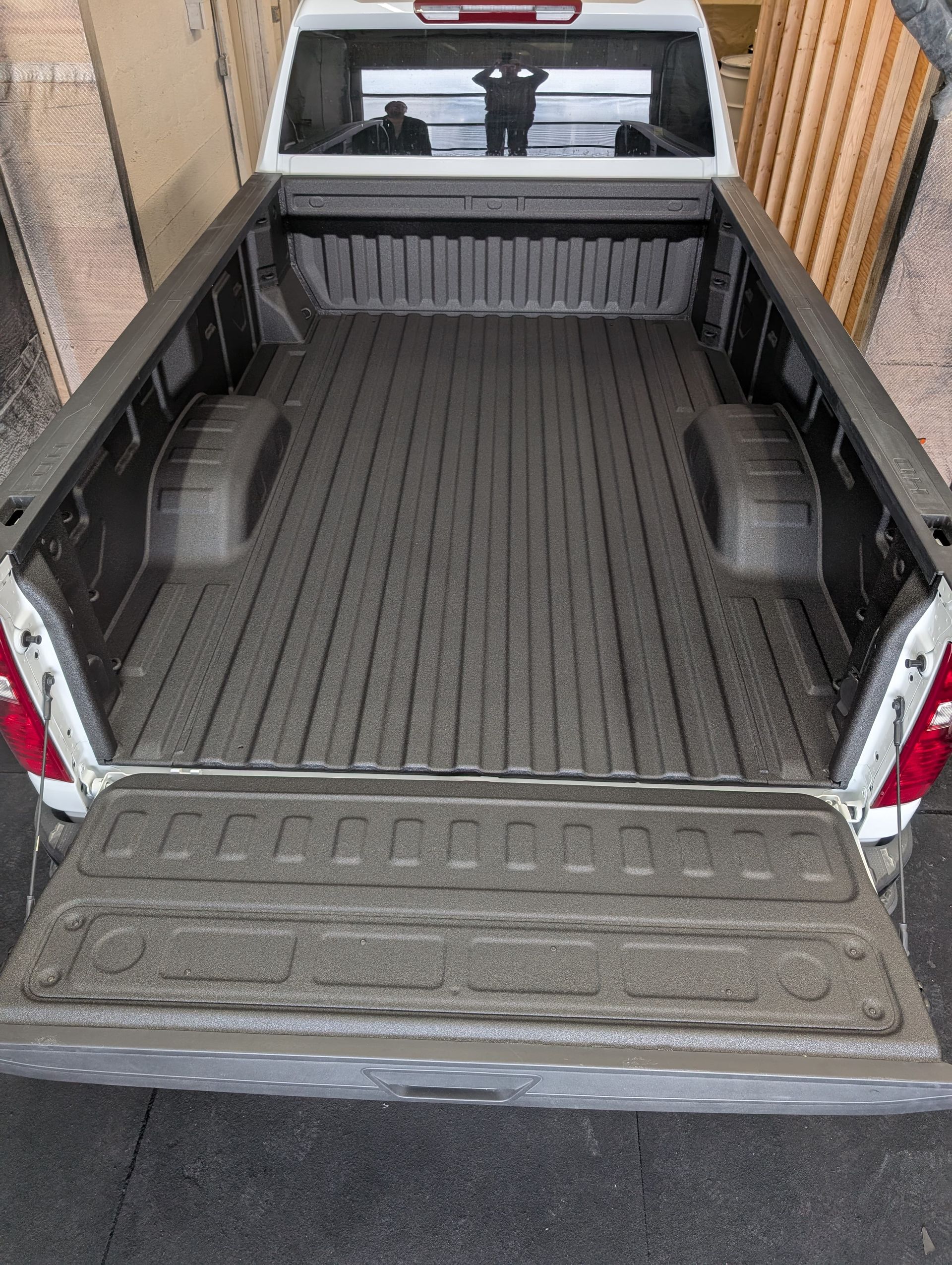 Open bed of a white pickup truck with a textured gray spray-in bedliner.