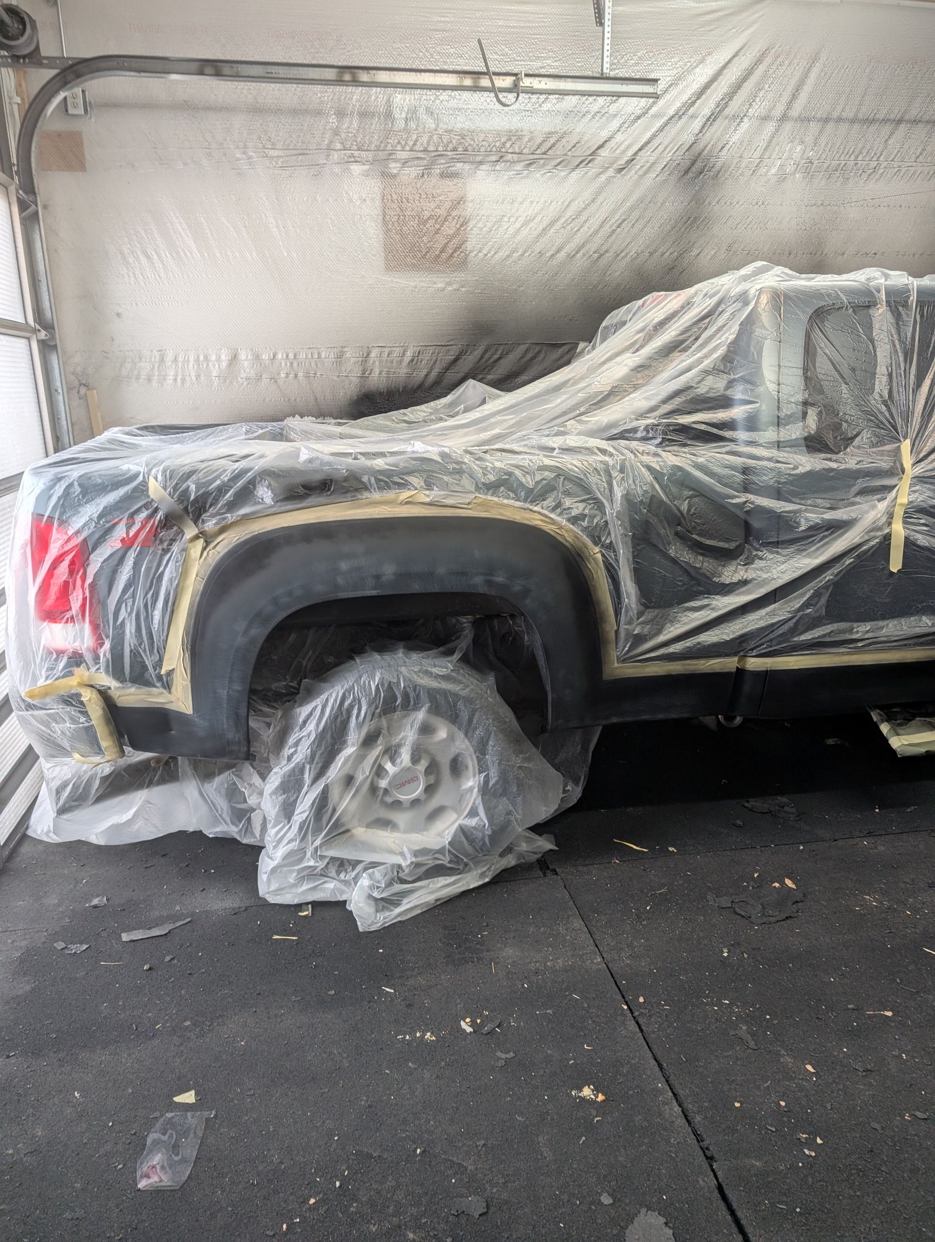 A black truck covered in plastic sheeting, masked for painting in a garage.