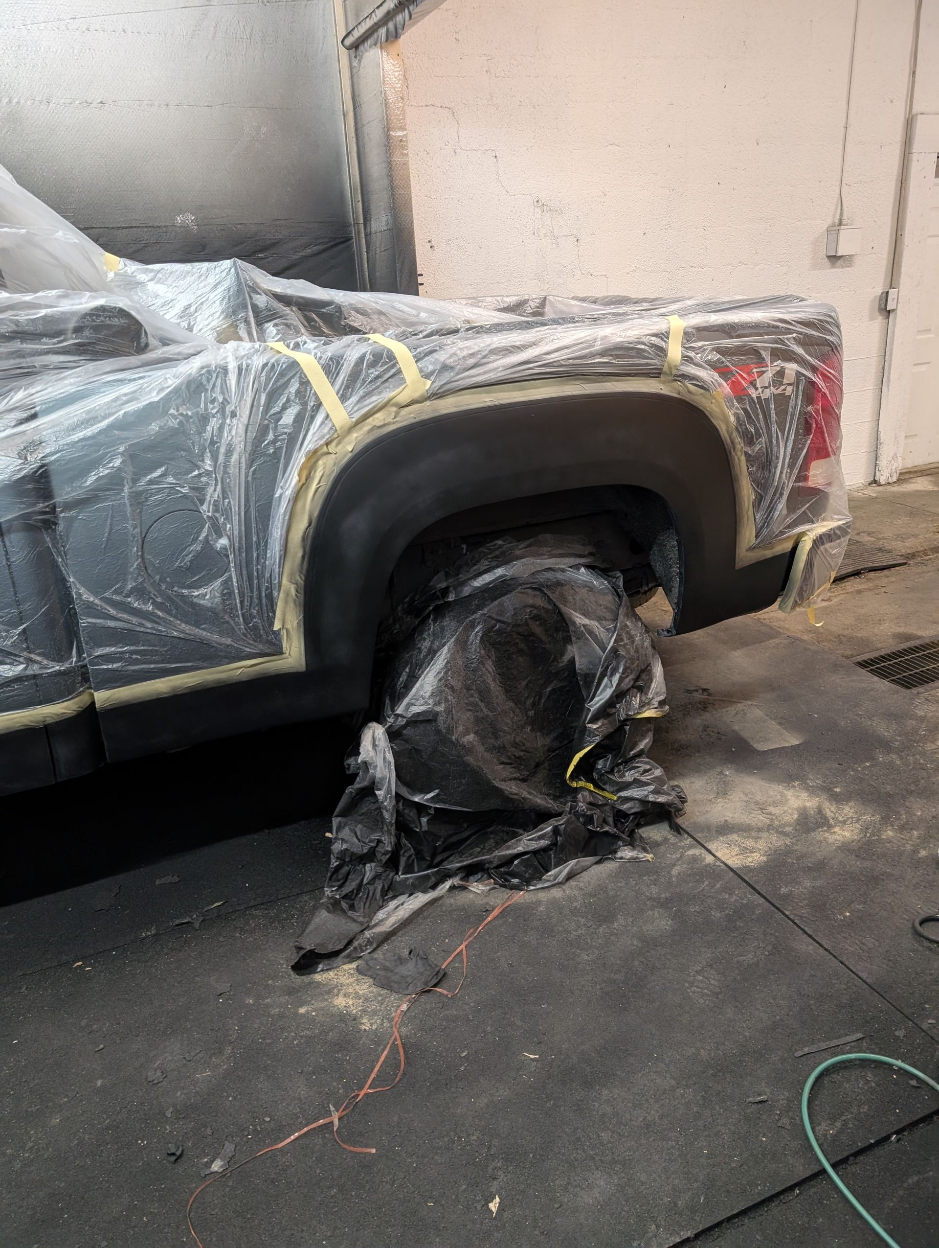 Black pickup truck prepared for paint; rear wheel covered, taped and masked.