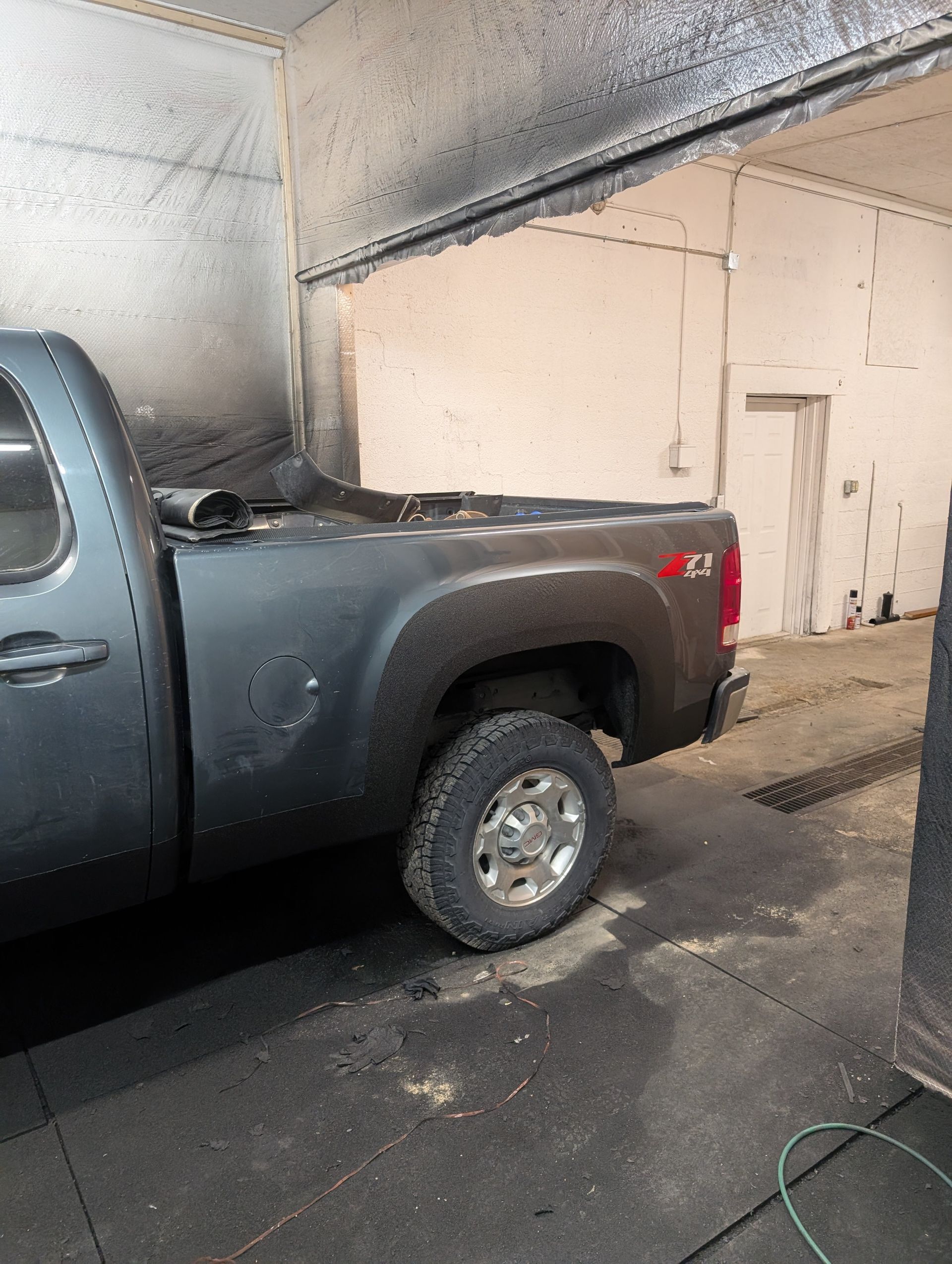 Gray Chevy pickup truck in a workshop, covered in black dust.