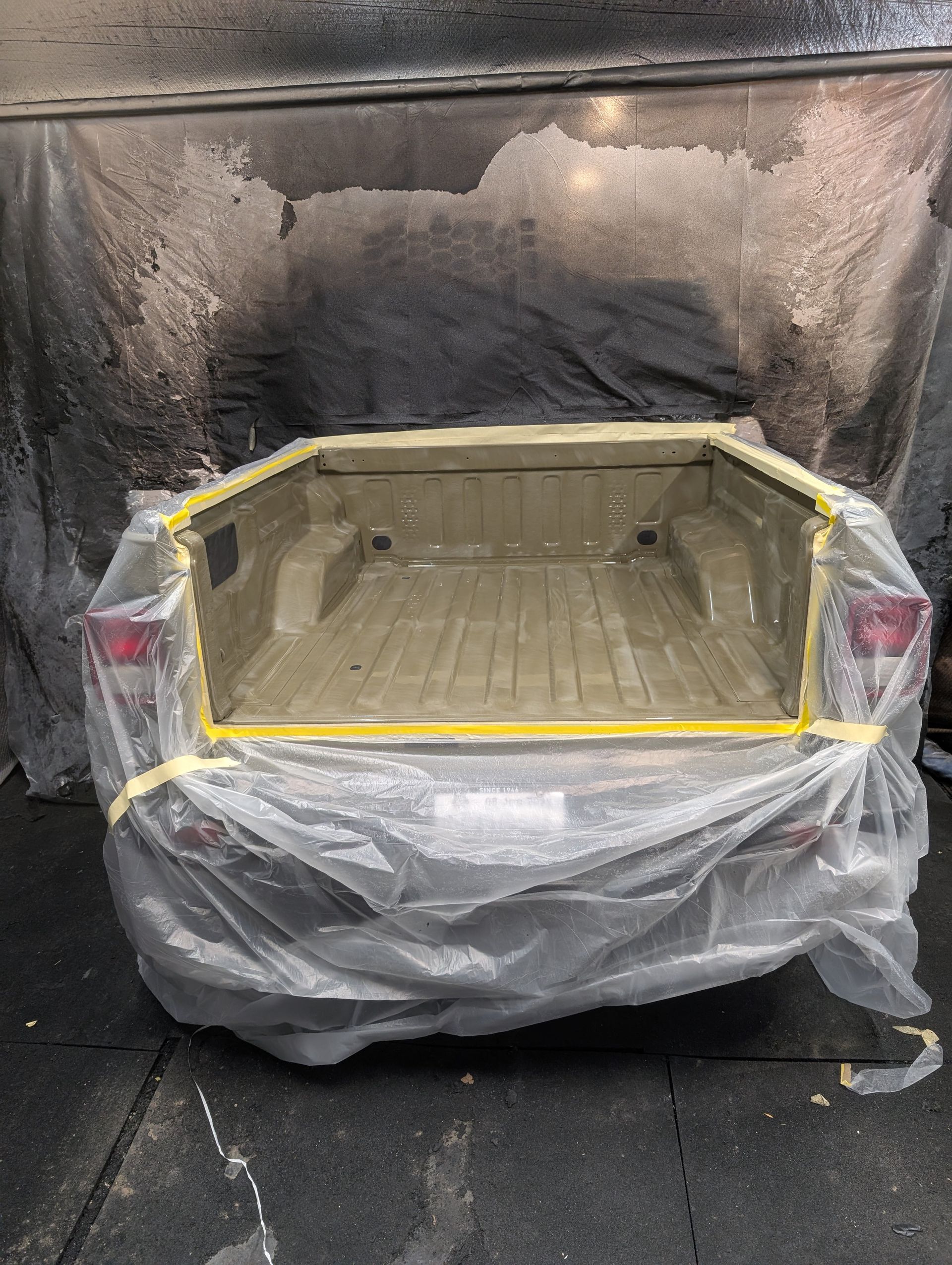 Truck bed masked with tape and plastic, ready for paint. Spray booth background.