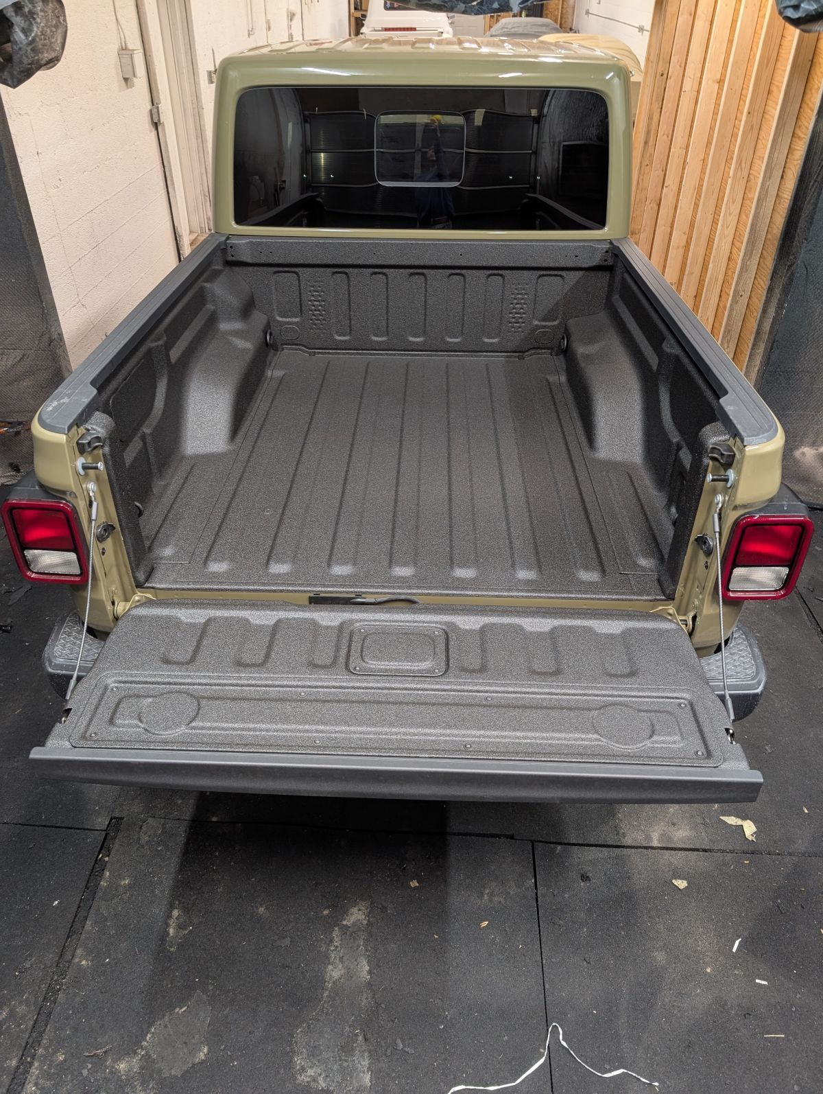 Open bed of a tan Jeep Gladiator pickup truck with a bedliner. Rear view.