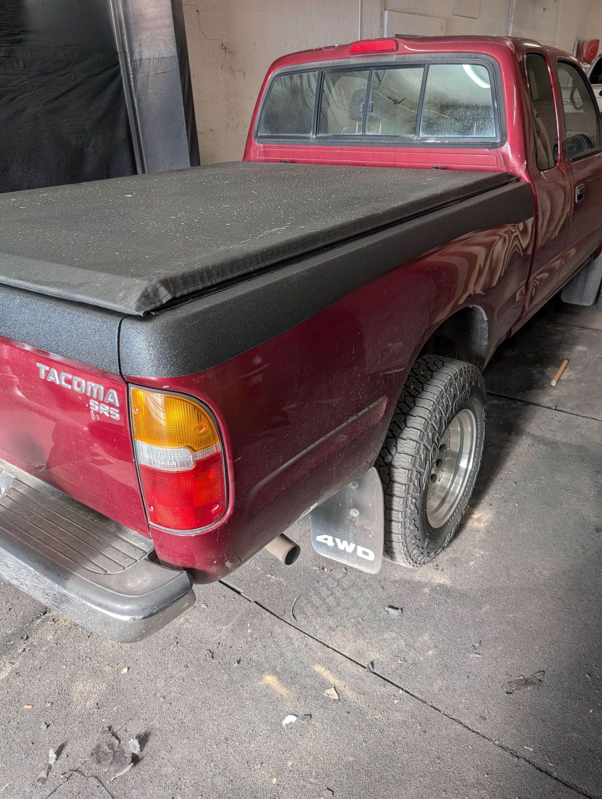 Red Toyota Tacoma pickup truck with a black bed cover, parked indoors.