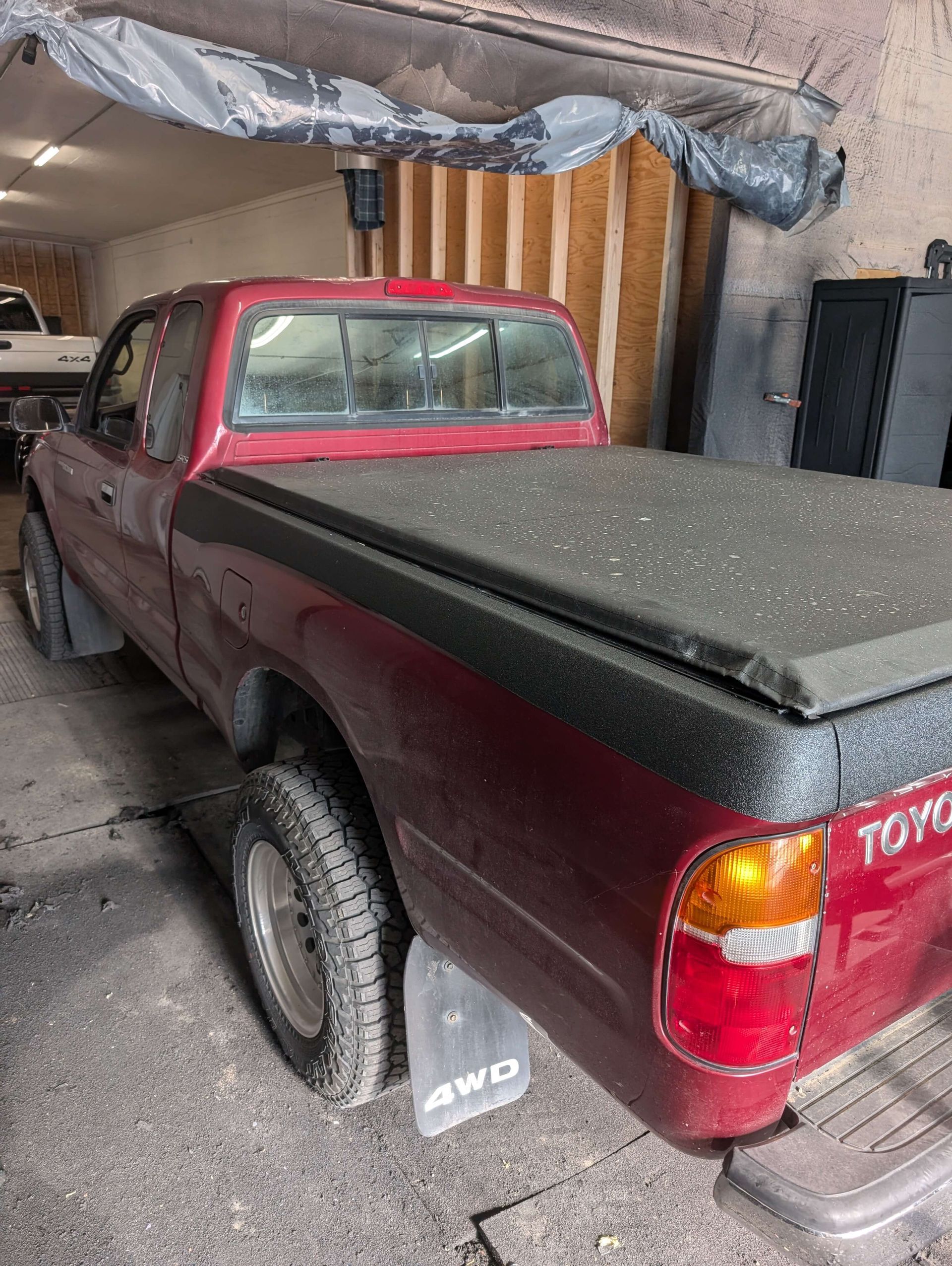 Red Toyota Tacoma truck with a black bed cover, parked in a garage.