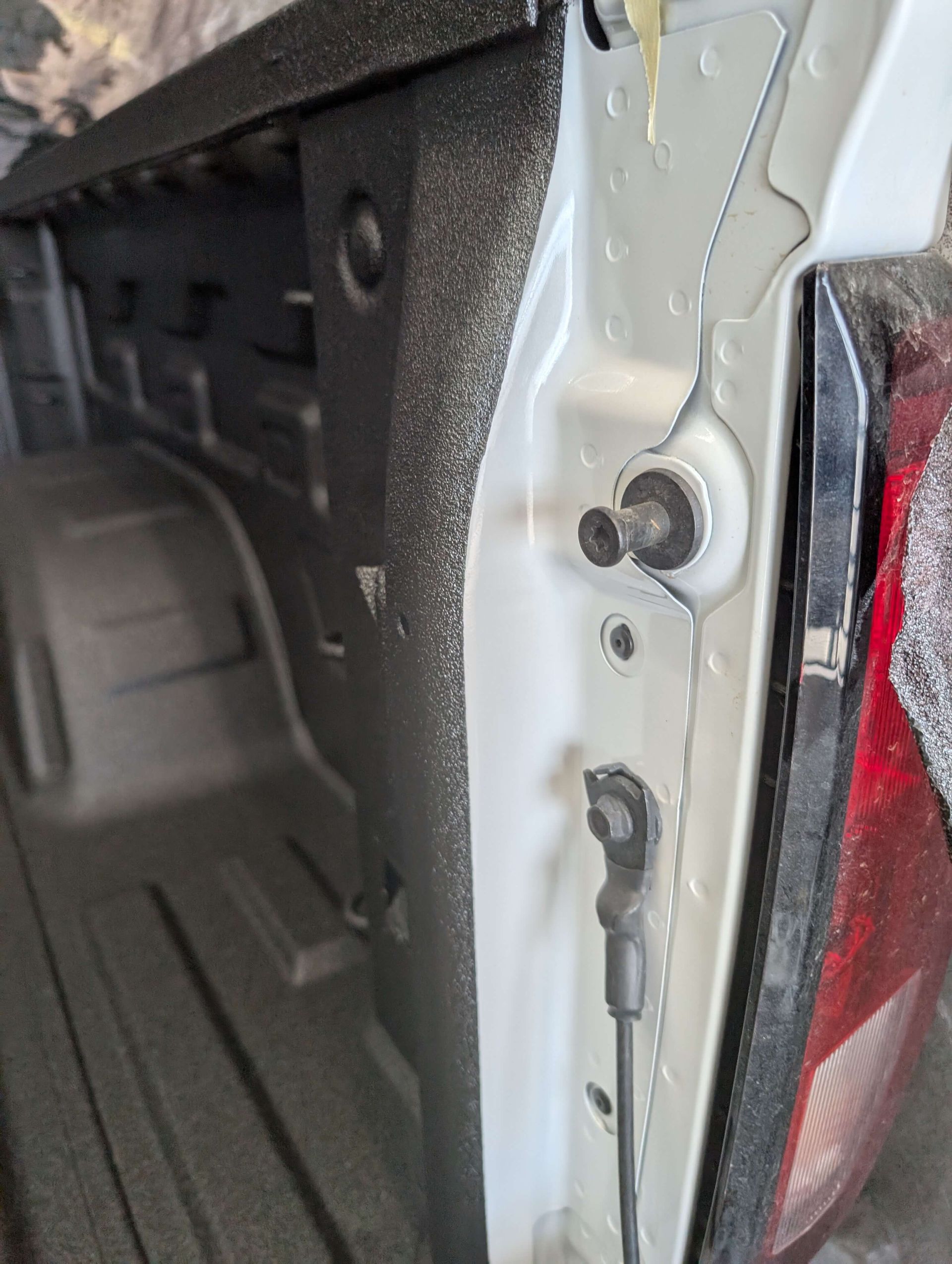 Close-up of a white truck bed interior, including a taillight. Black bed liner, hardware visible.