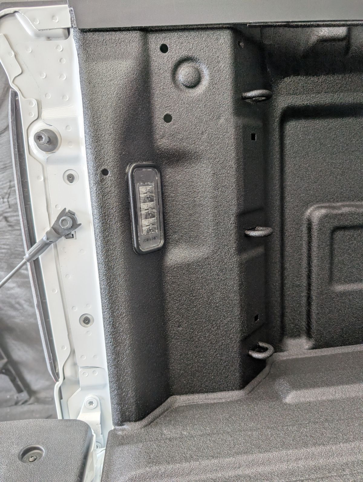 Close-up of a textured truck bed interior. A small control panel is mounted to a black-coated side panel.