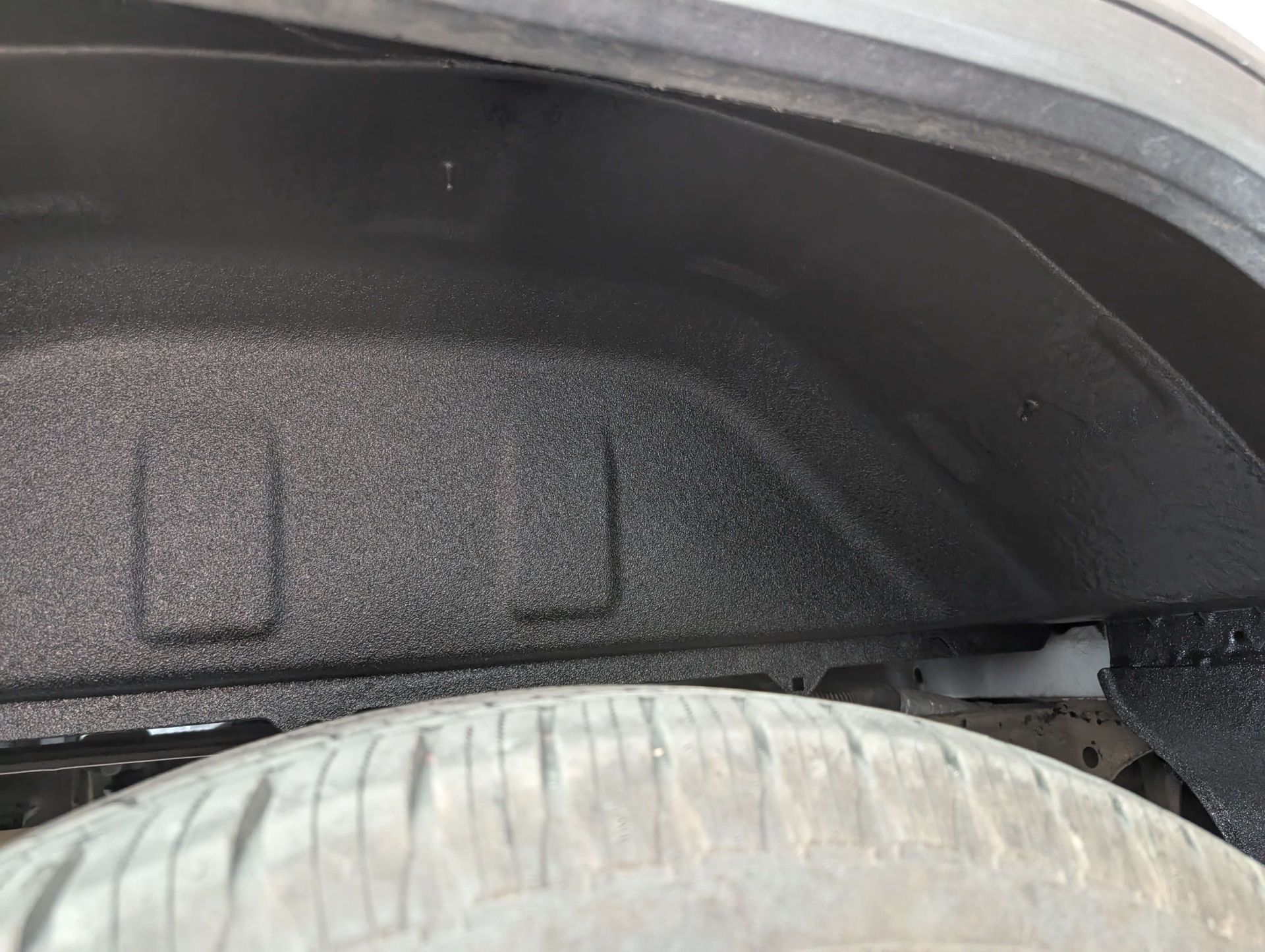 Black textured coating inside a truck wheel well, covering metal. Tire visible below.