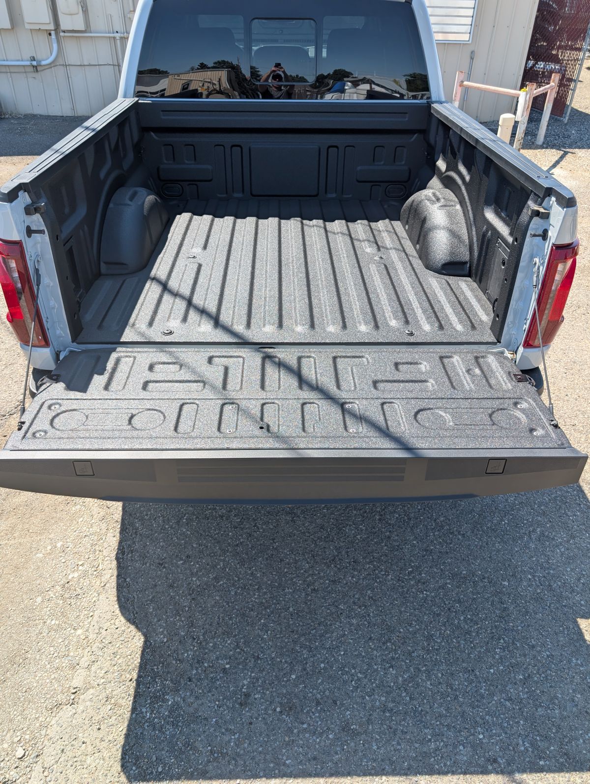 Rear view of a white pickup truck with a black textured bed and open tailgate.