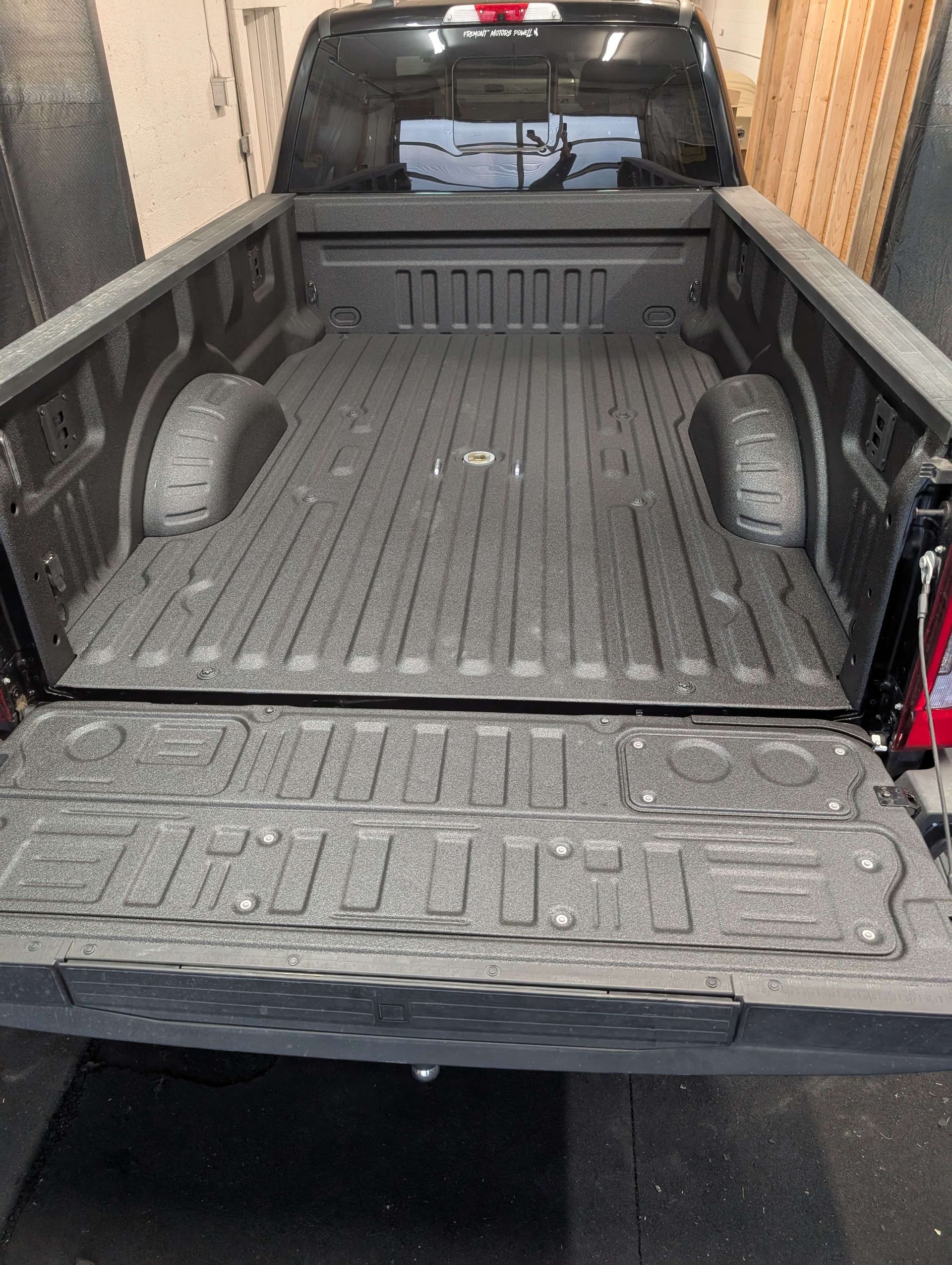 Truck bed with black spray-on bedliner, showing the tailgate down.