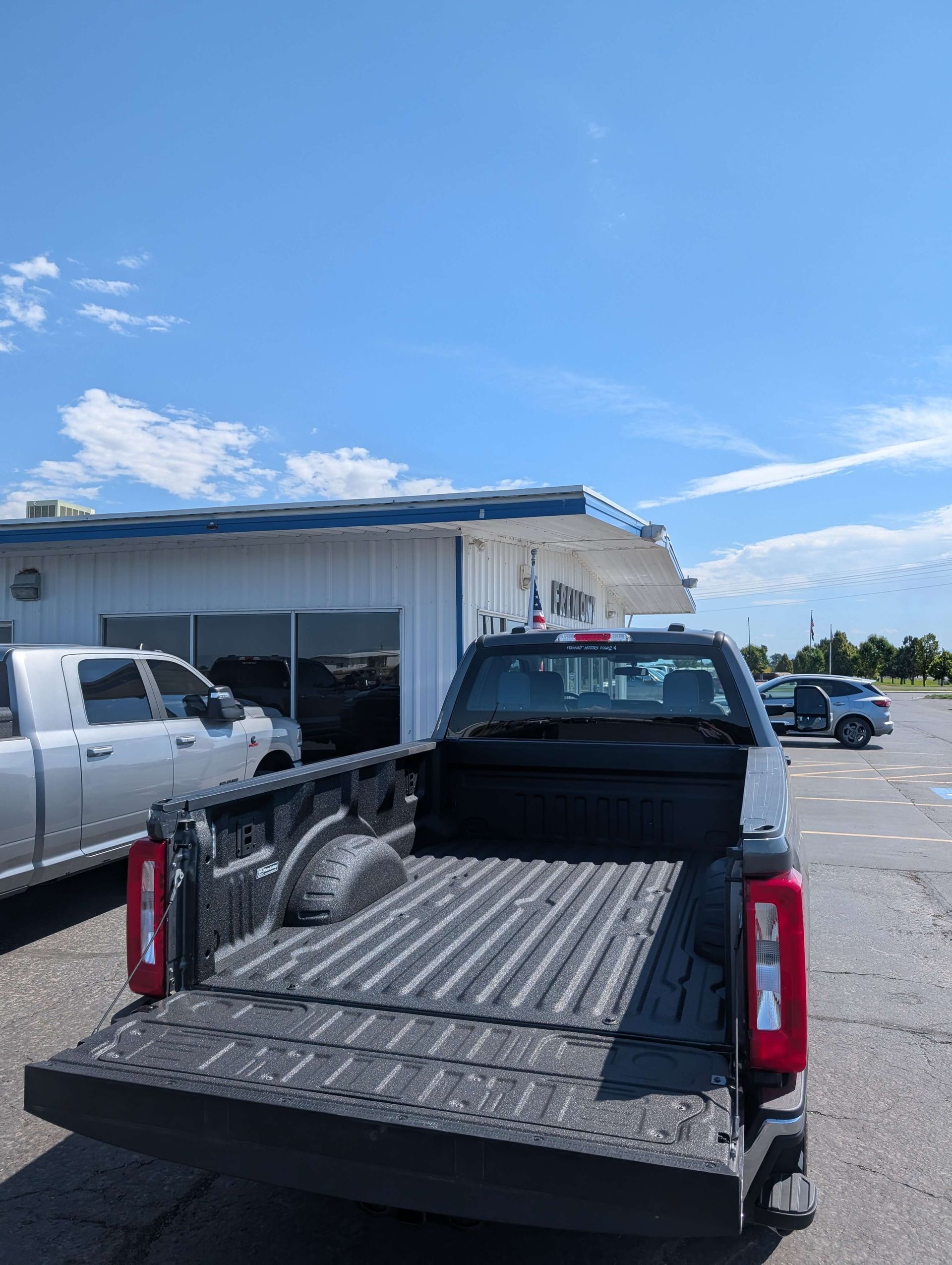 Black pickup truck with open bed at a dealership on a sunny day.