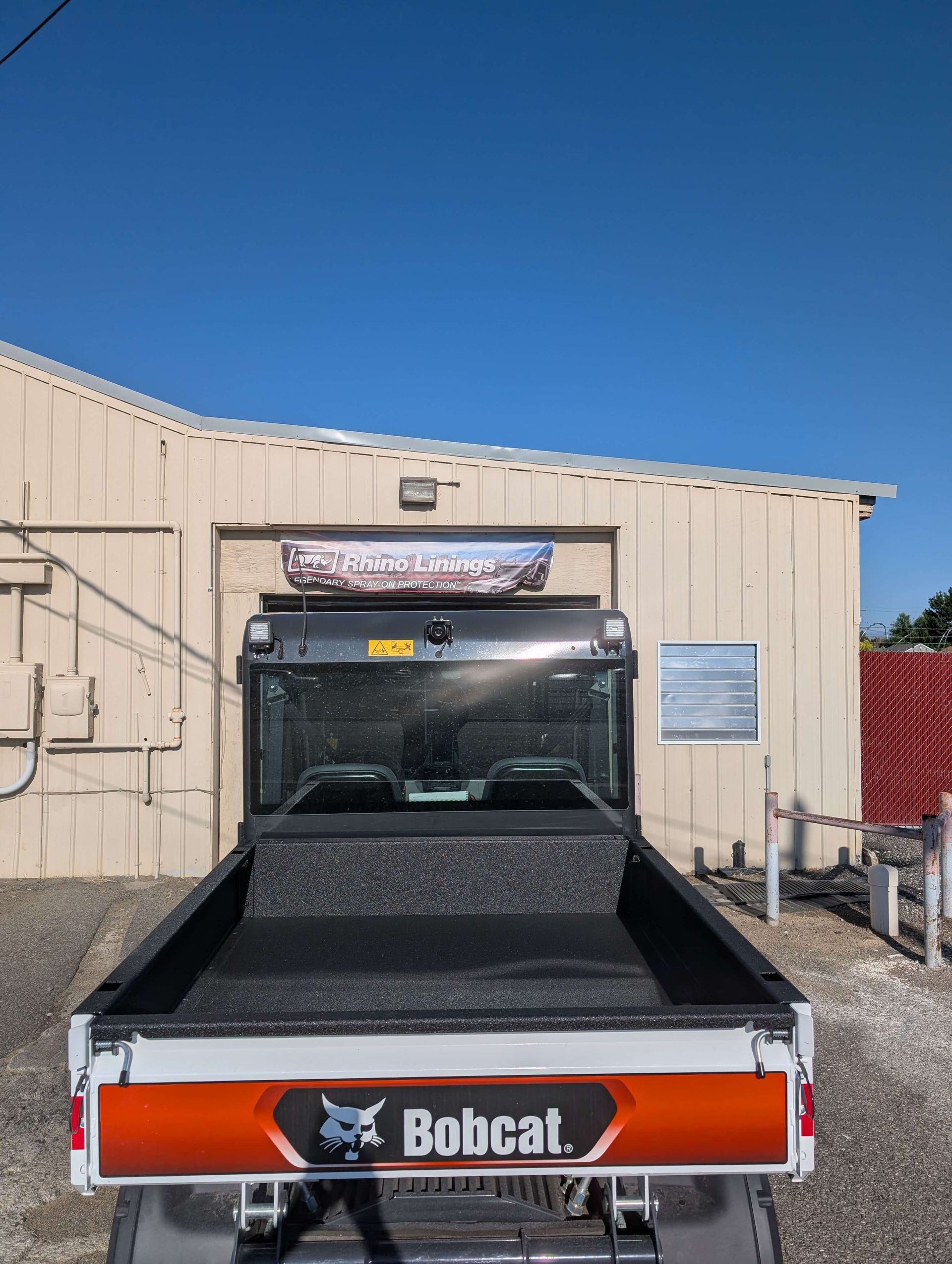 Bobcat utility vehicle parked in front of a building, blue sky overhead.