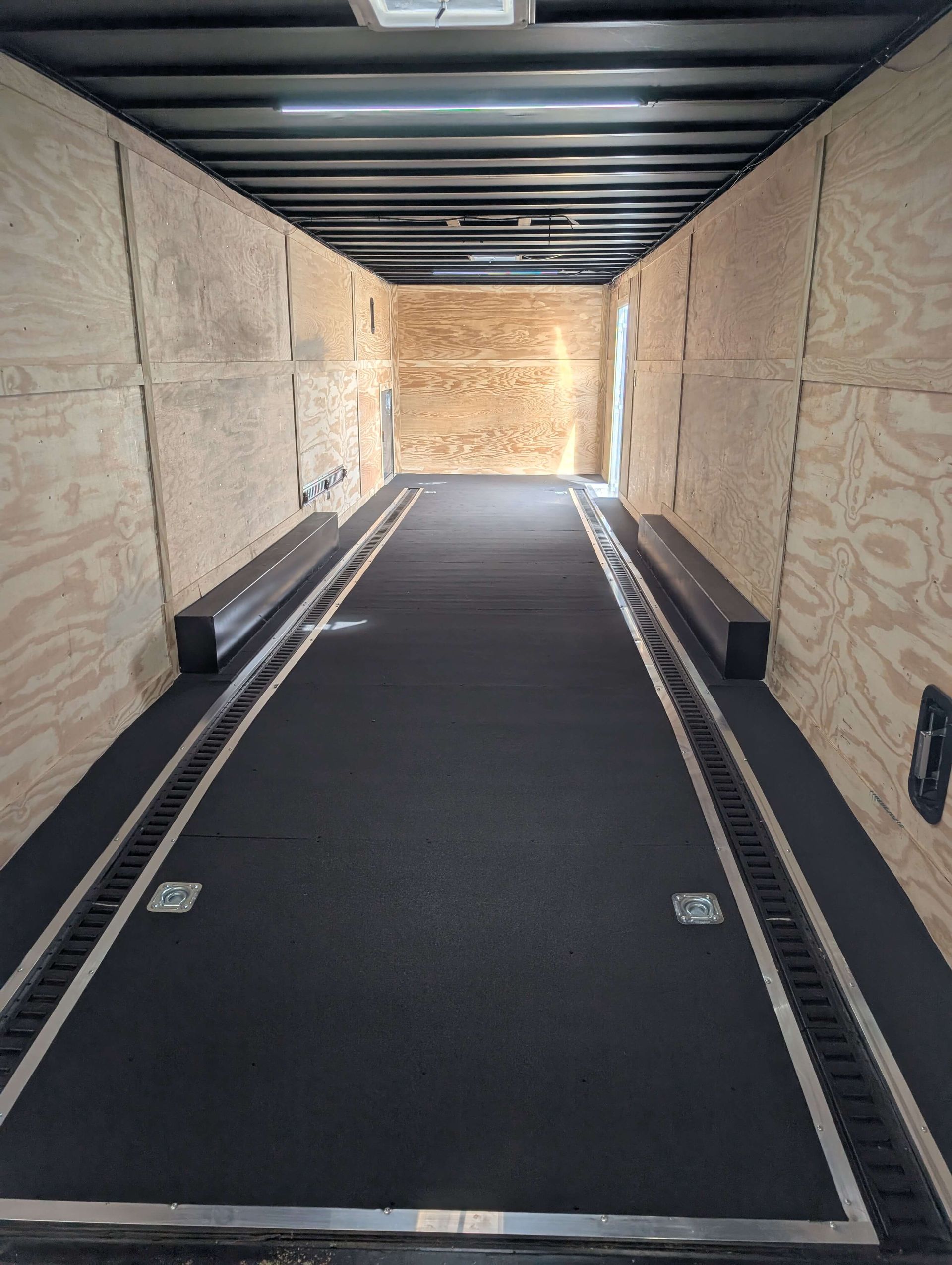 Interior of an empty cargo trailer with wood panel walls, black floor, and tie-down tracks.