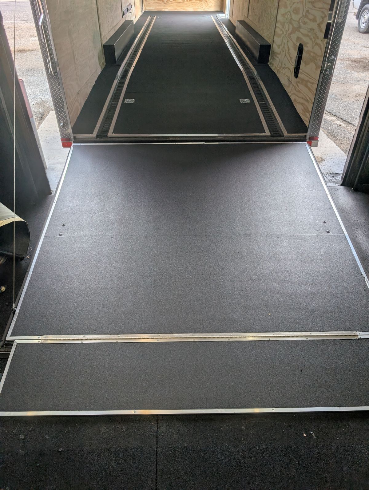Inside of a cargo trailer with a black rubber floor and a ramp at the back for loading.
