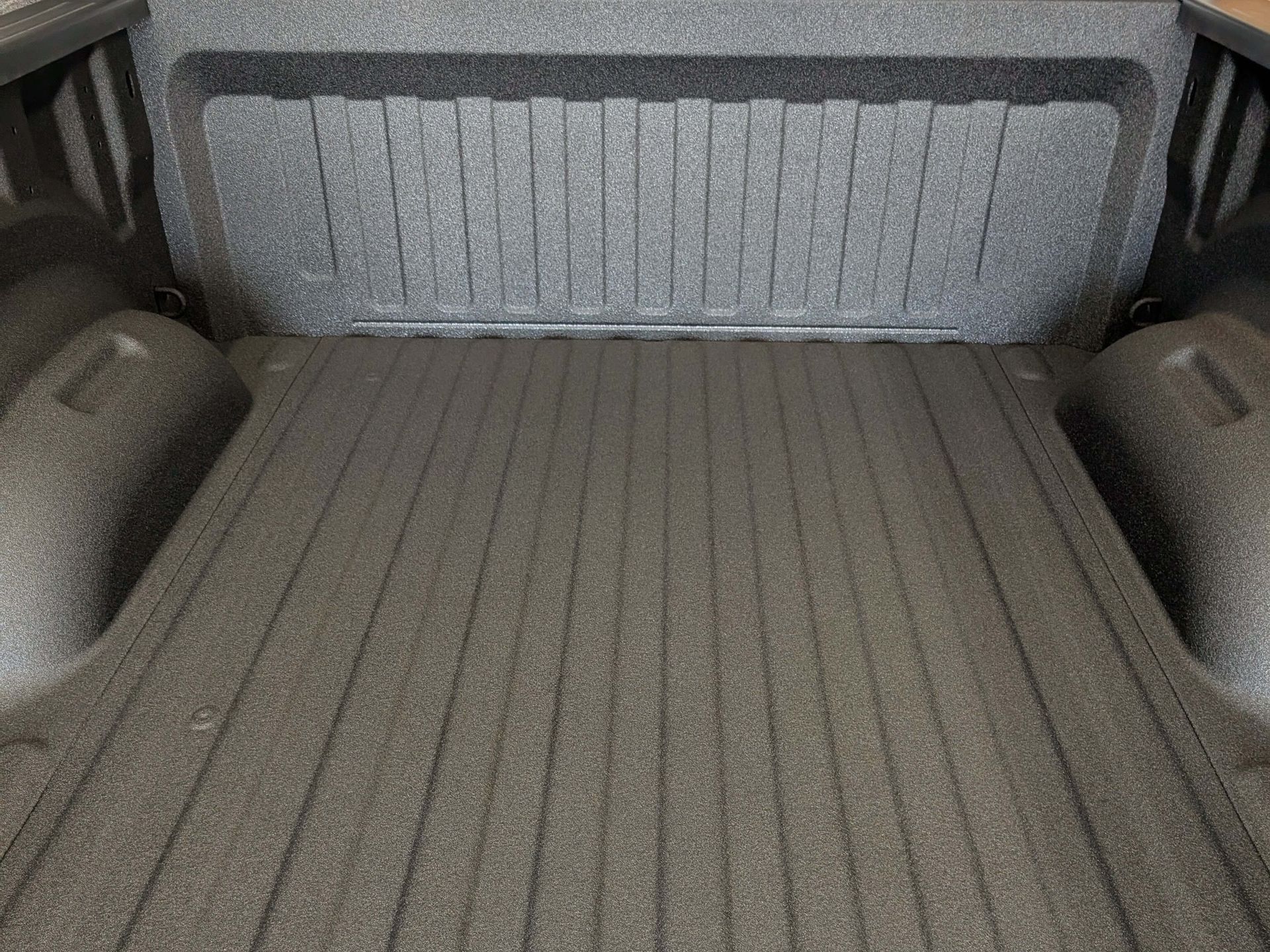 Black truck bed interior with ribbed floor and textured sidewalls and rear.