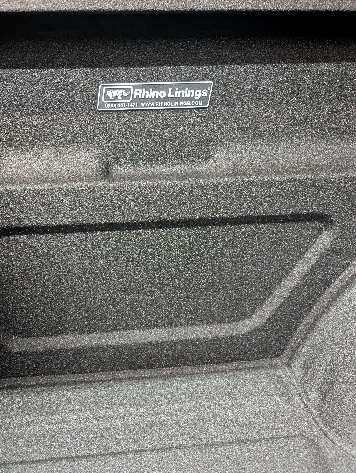 Rhino Linings truck bed liner, textured black, with logo.