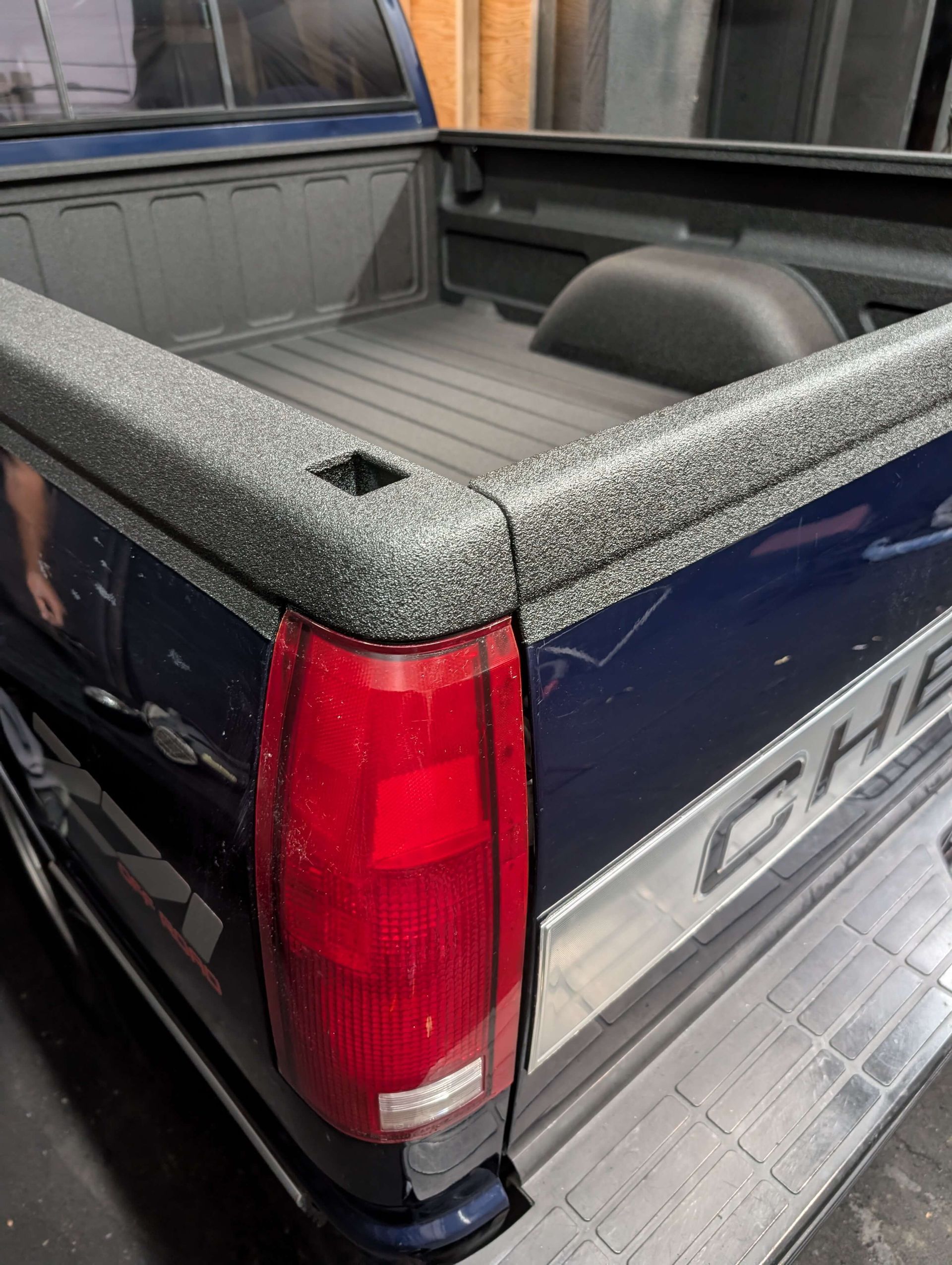 Blue Chevrolet pickup truck bed with a textured black and silver bedliner.