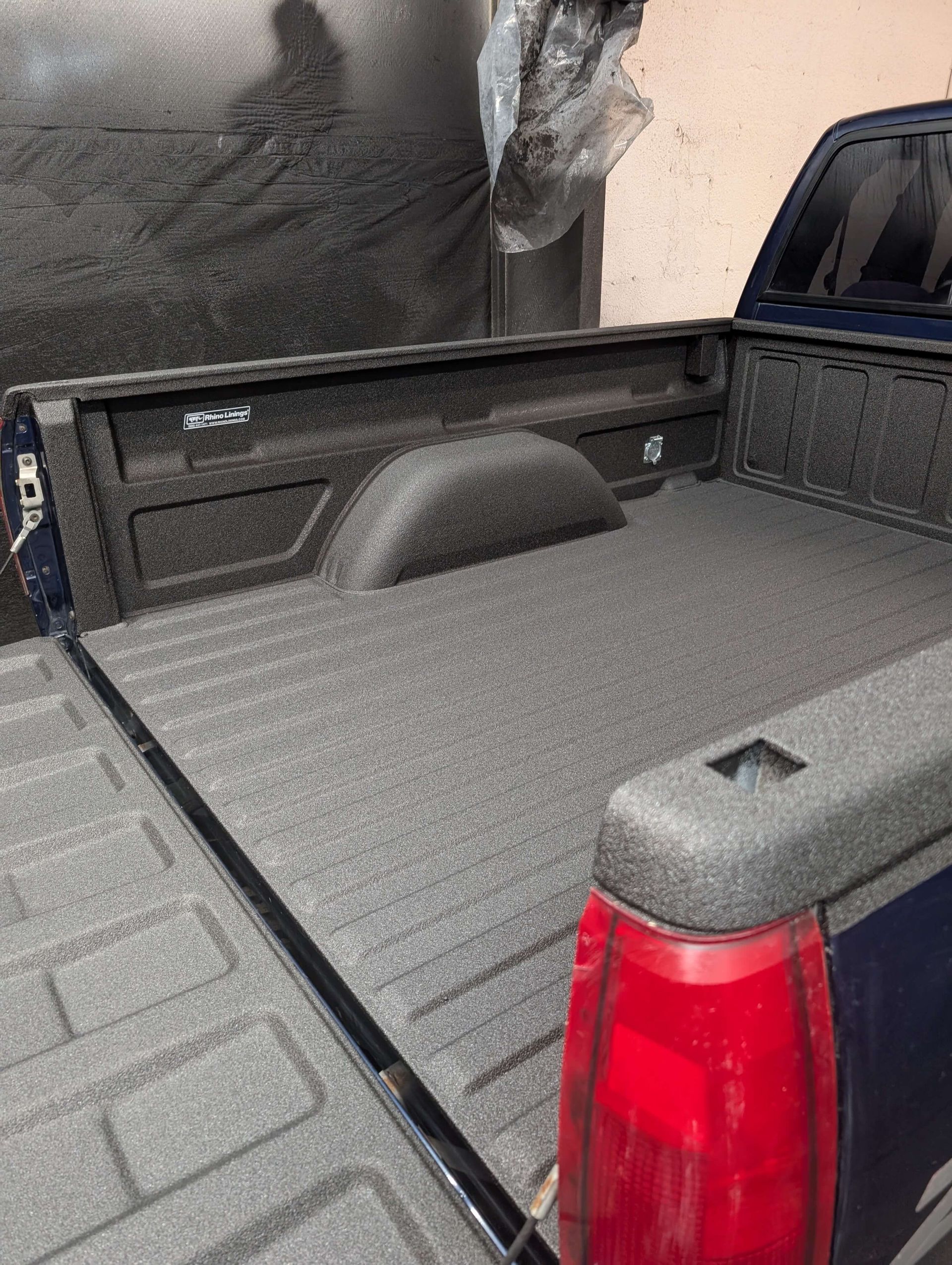 Truck bed with a dark, textured spray-on bed liner. Tail light visible.