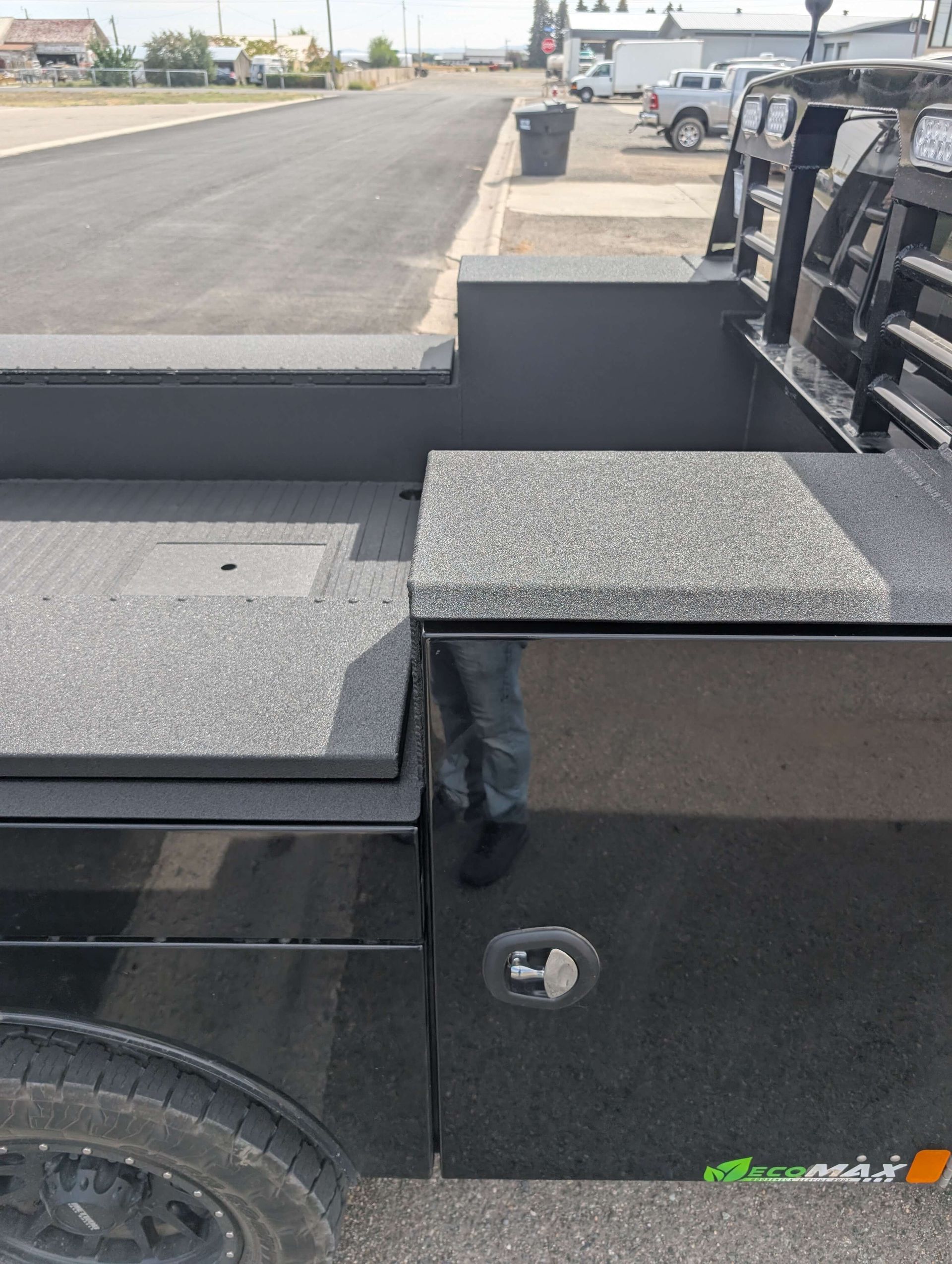 Black truck bed with storage compartments and textured surfaces, parked on a street.