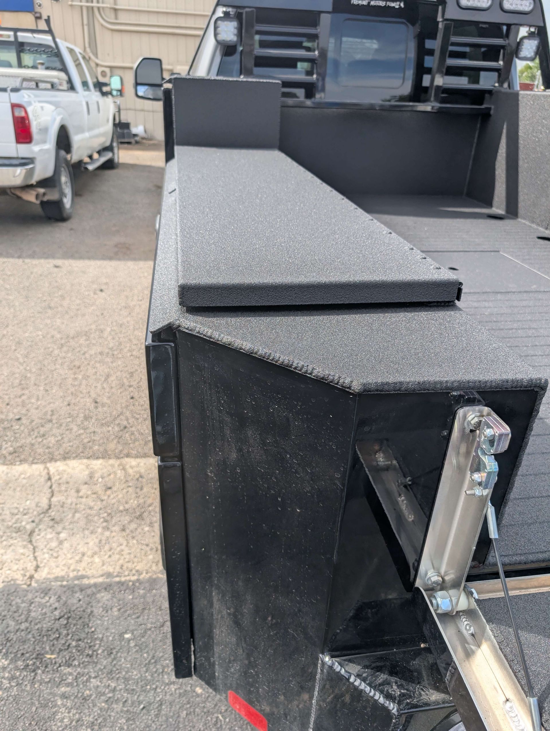 Black truck bed with textured surface, near a white truck.