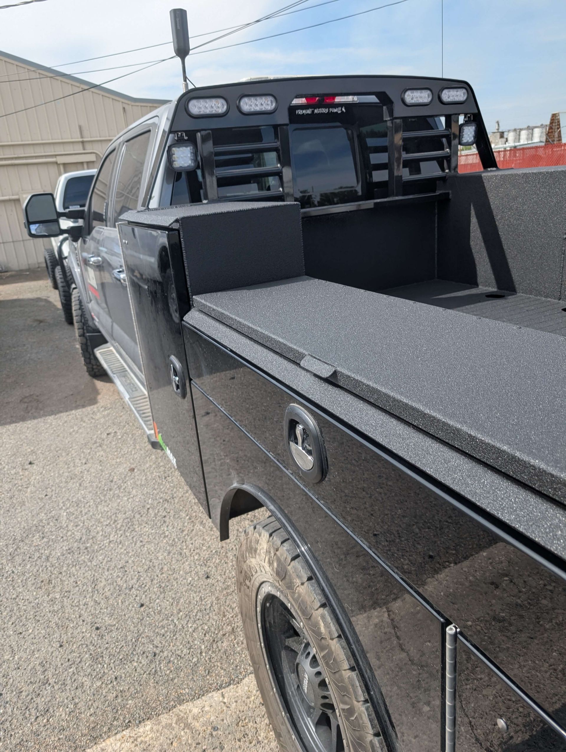 Black flatbed truck with storage compartments, antenna, and work lights.
