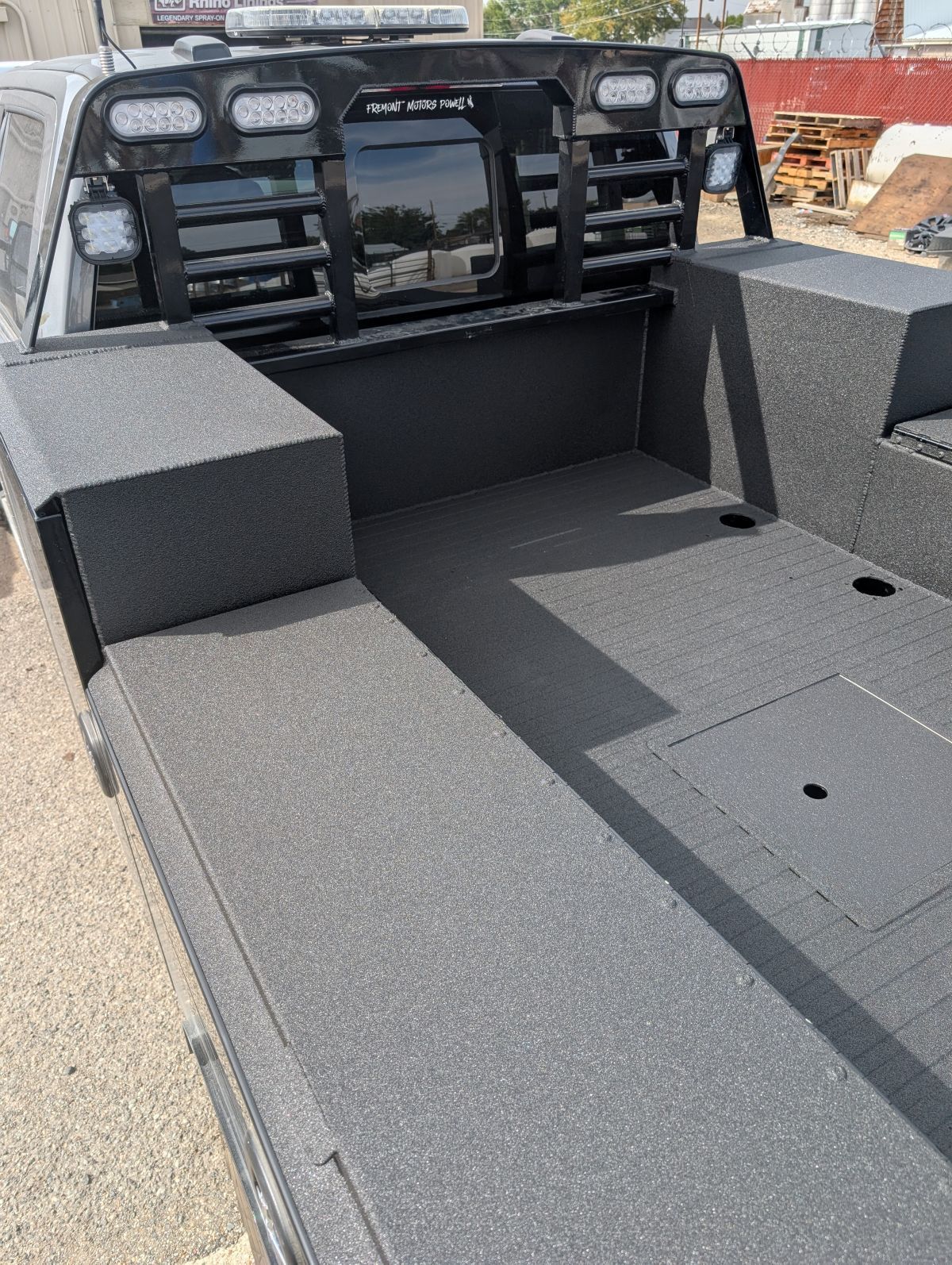 Black truck bed with textured coating. Features headboard with lights and side storage compartments.