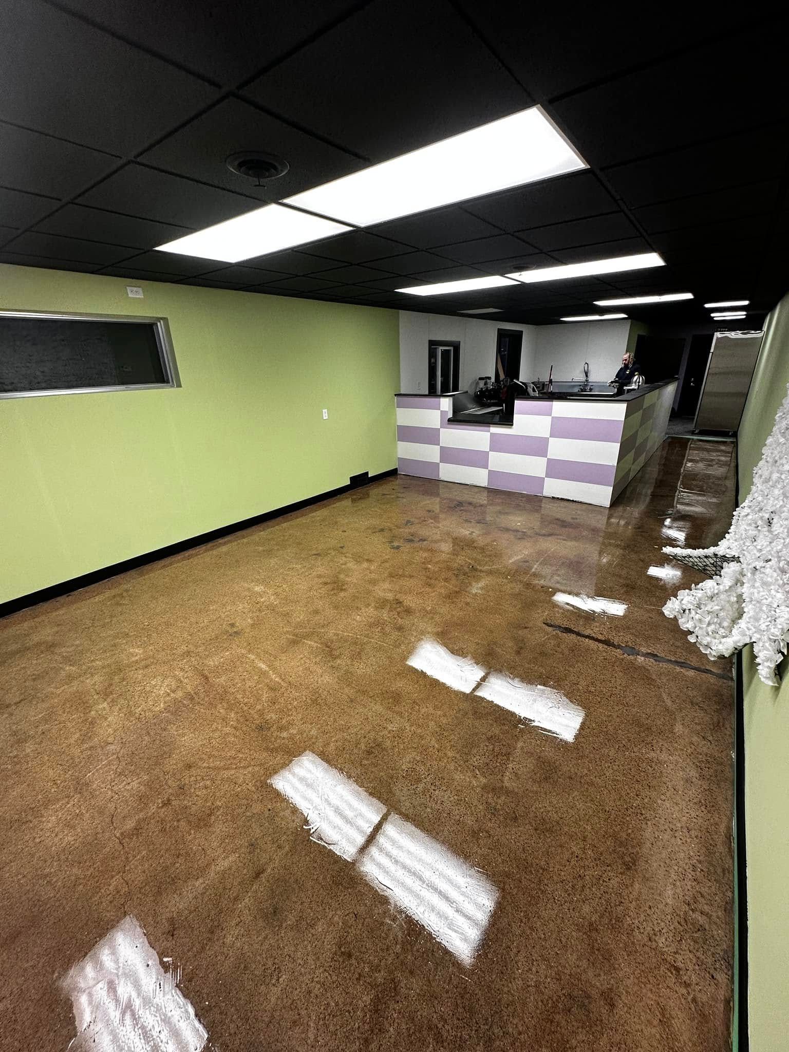Empty retail space with stained concrete floor, light green walls, checkered counter, and black ceiling.
