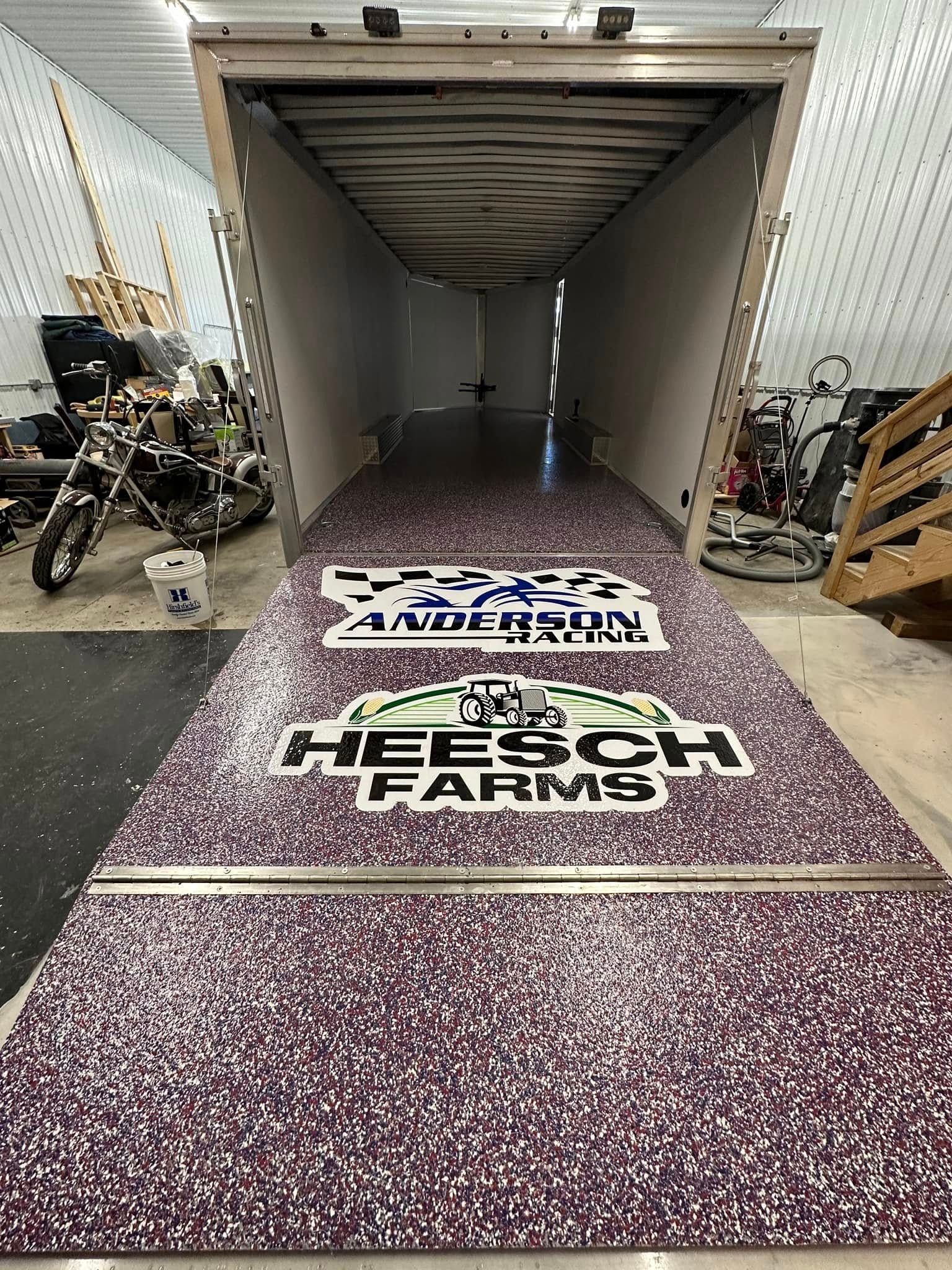 Inside a trailer with a speckled floor, Anderson Race and Heesch Farms logos are visible. Motorcycle and equipment clutter sides.