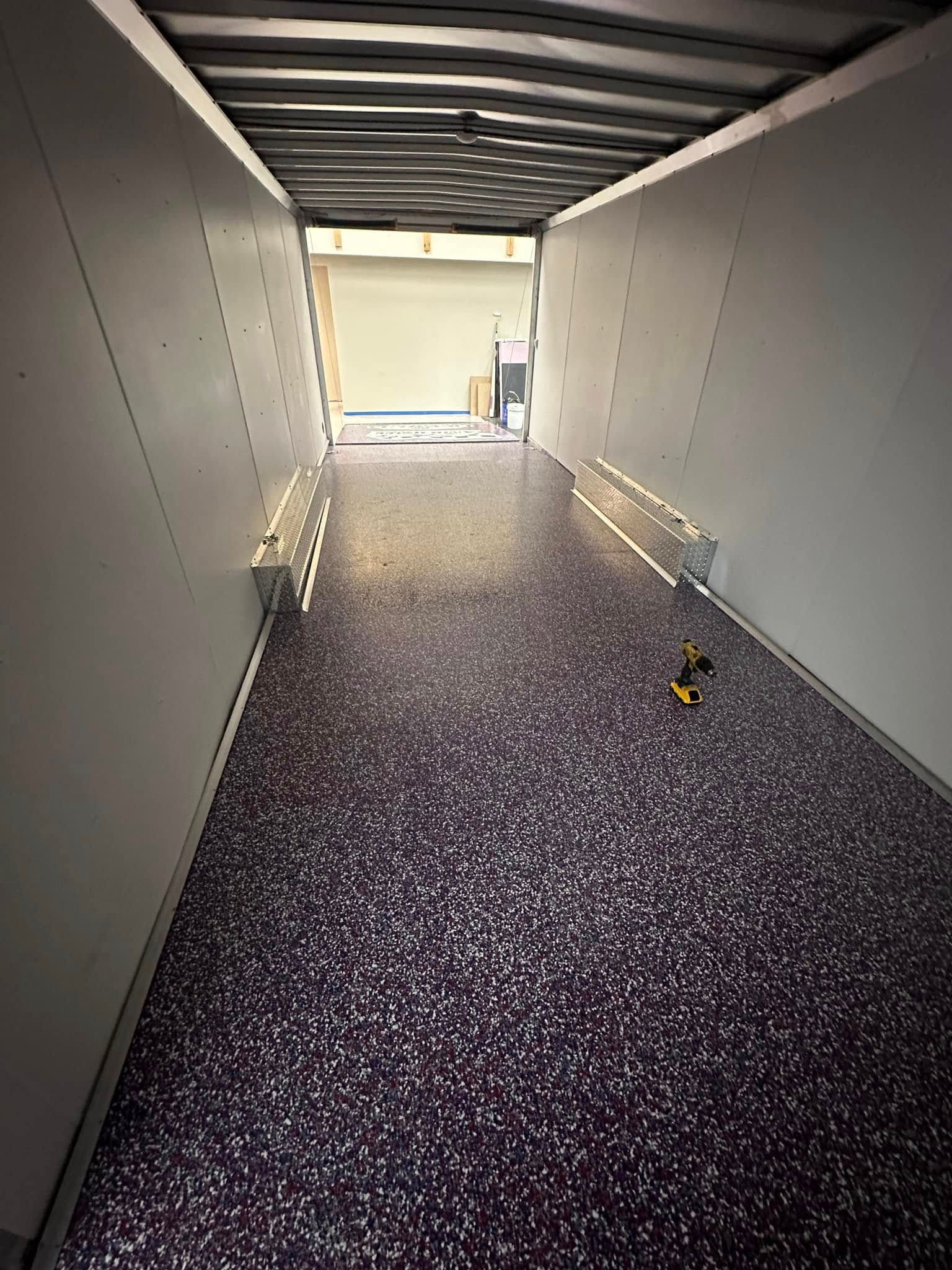 Inside a cargo trailer with white walls and a speckled purple floor, with open entrance in the distance.