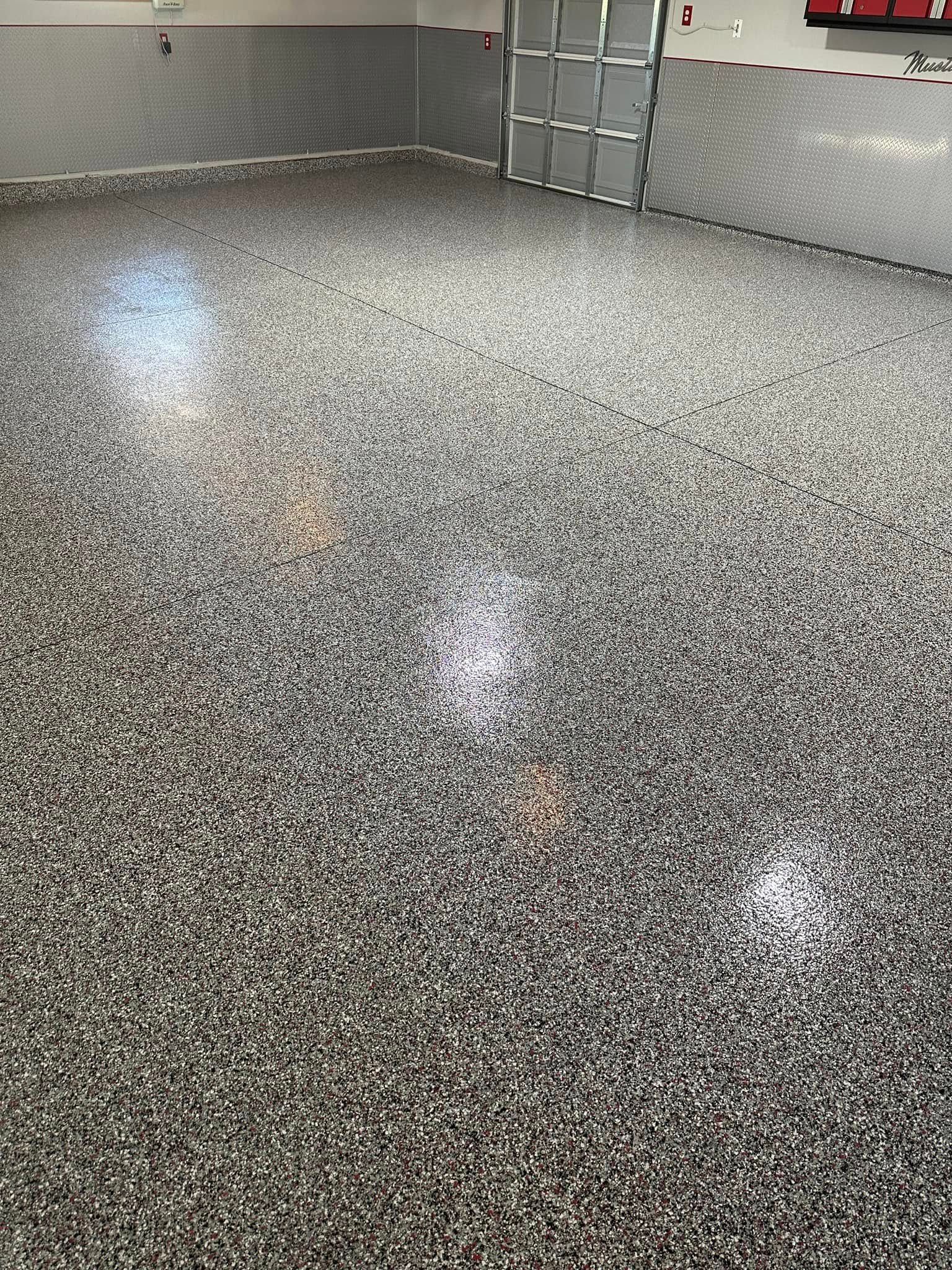 Garage with a speckled epoxy floor. The walls are gray. Light reflects off the floor.