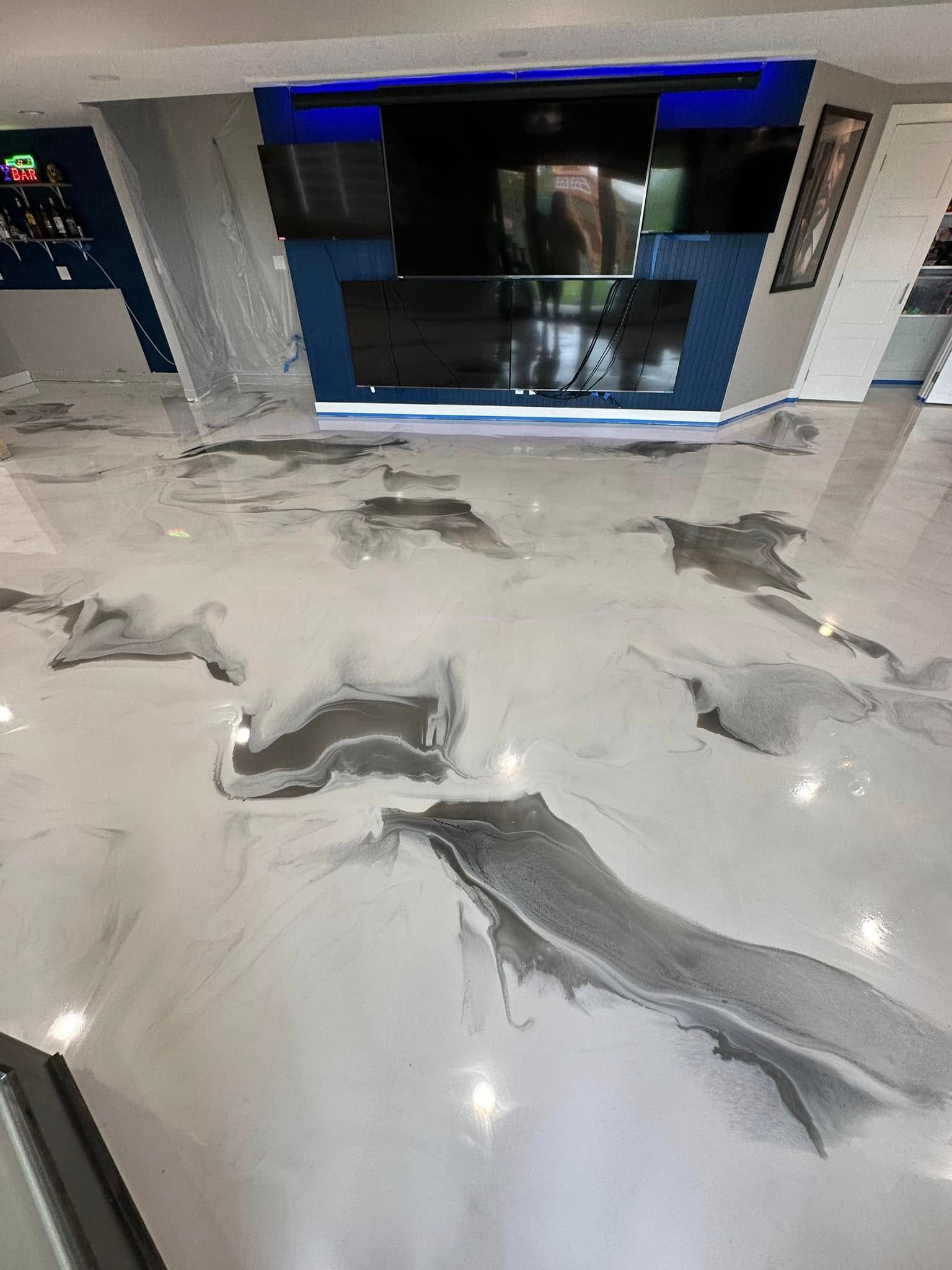 Shiny epoxy floor with silver and grey marbled design; TV and blue paneling in background.