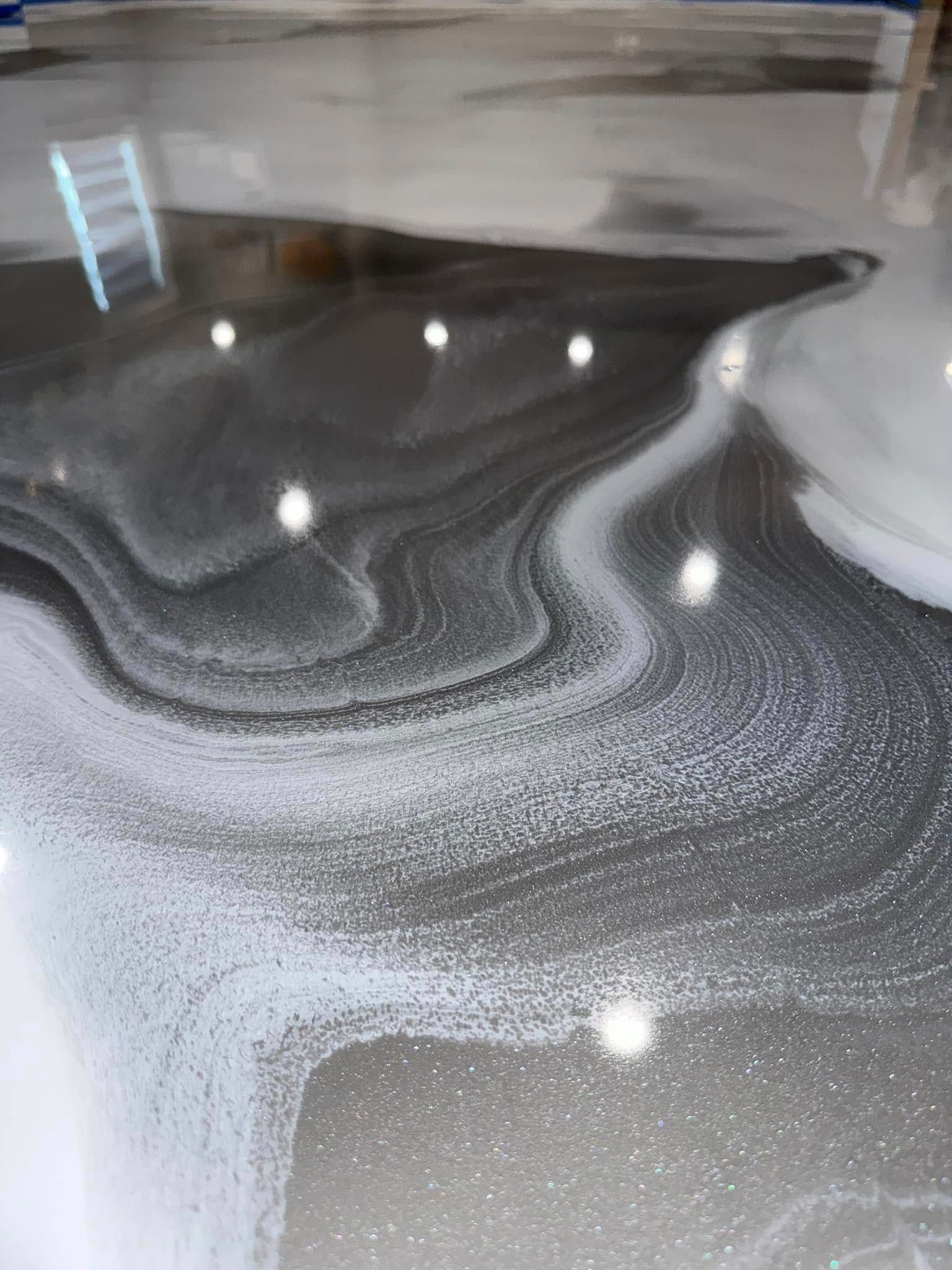 Swirled metallic epoxy floor with gray, white, and silver tones reflecting light.