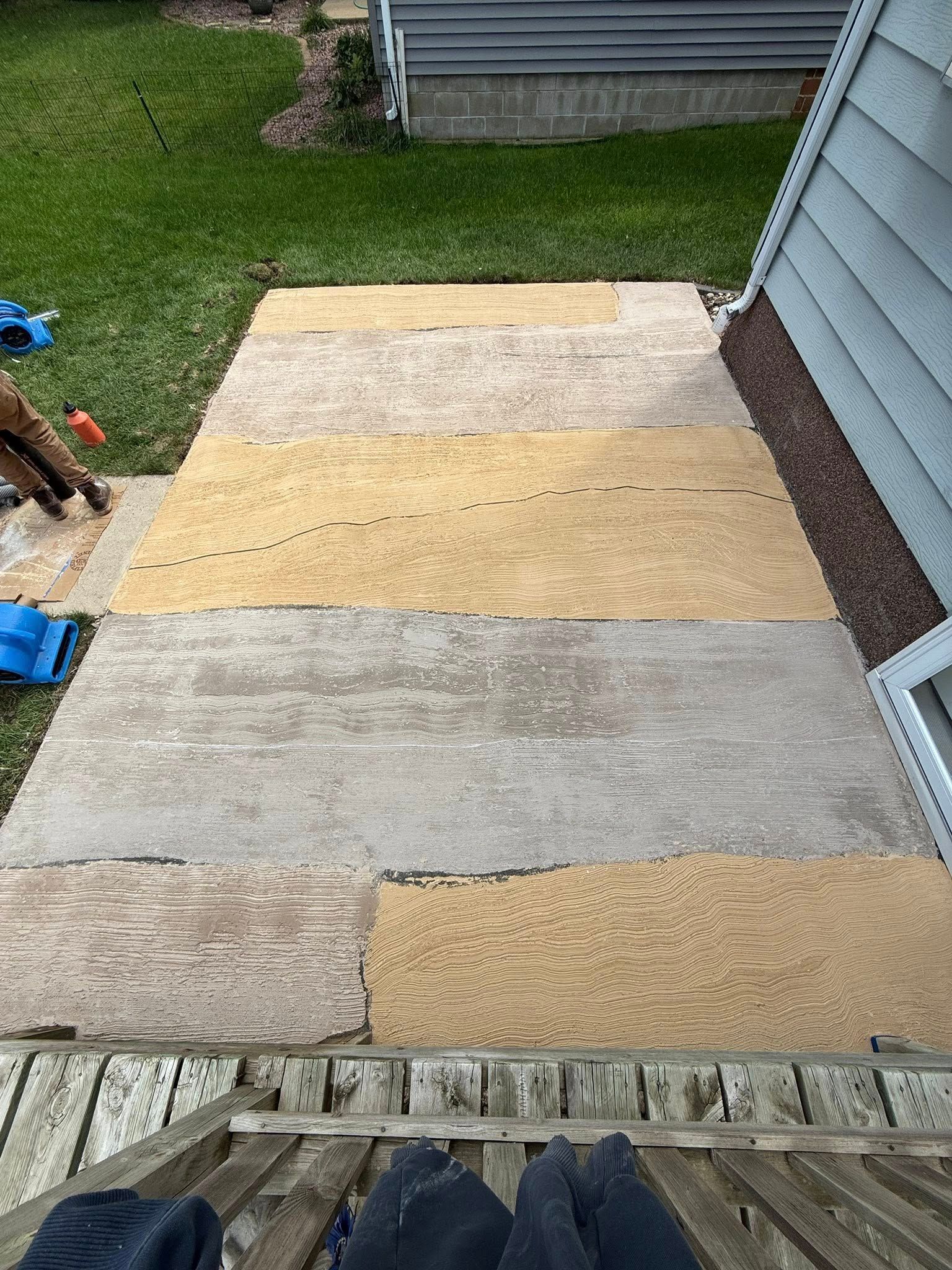 Pathway of tan and gray interlocking tiles, leading to a house. Footwear is visible on the stairs.