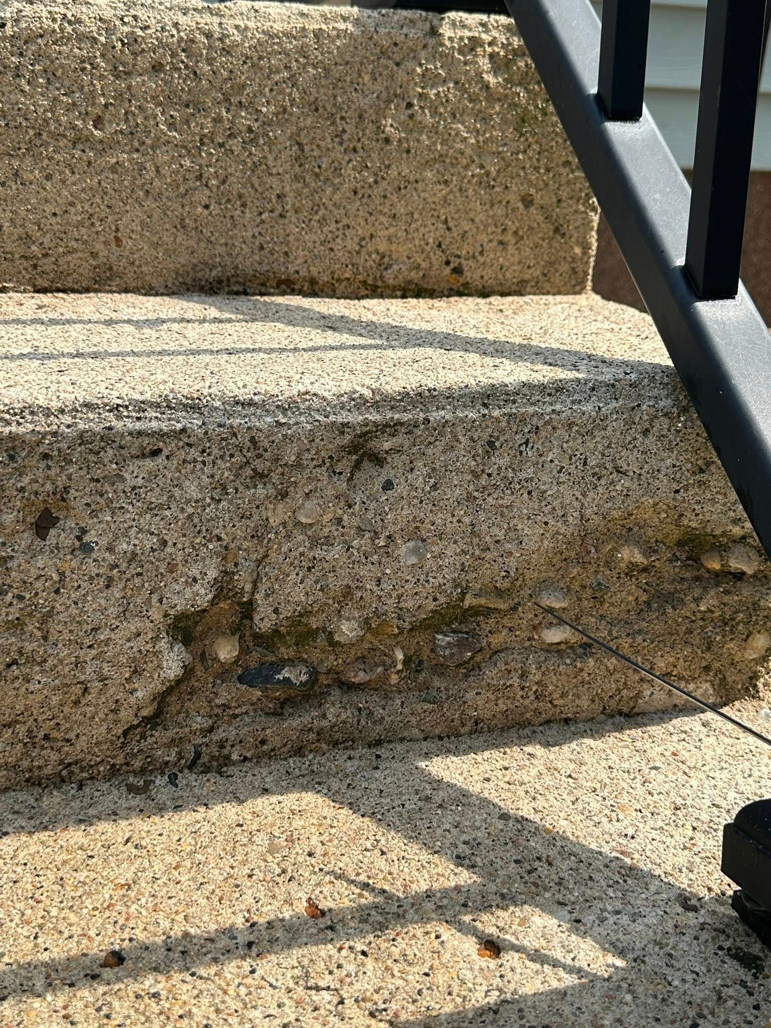Granite steps with damaged edges, with a black railing in the corner.