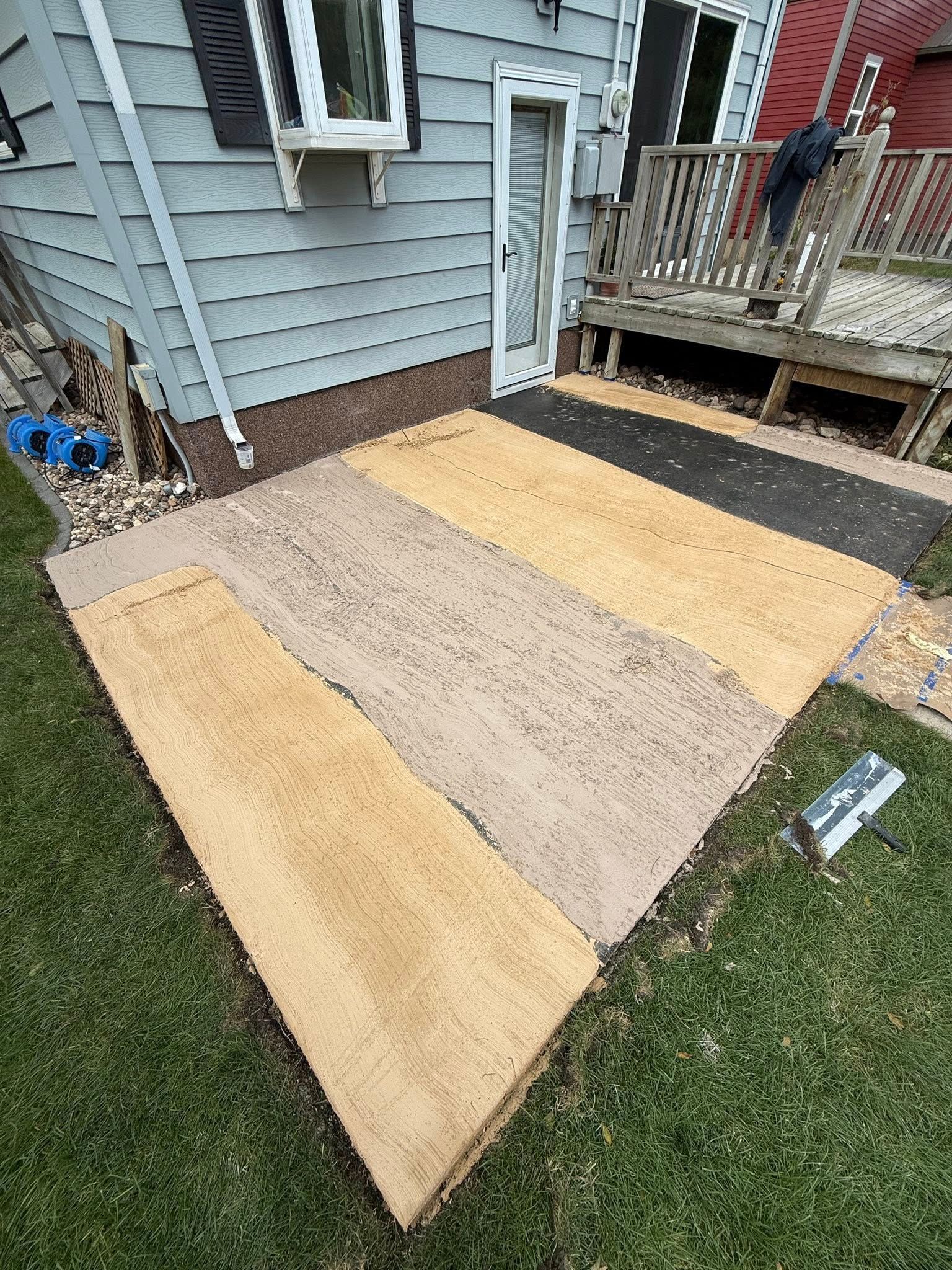 Concrete patio with varied textures and colors; a walkway leading to a house door and a deck.