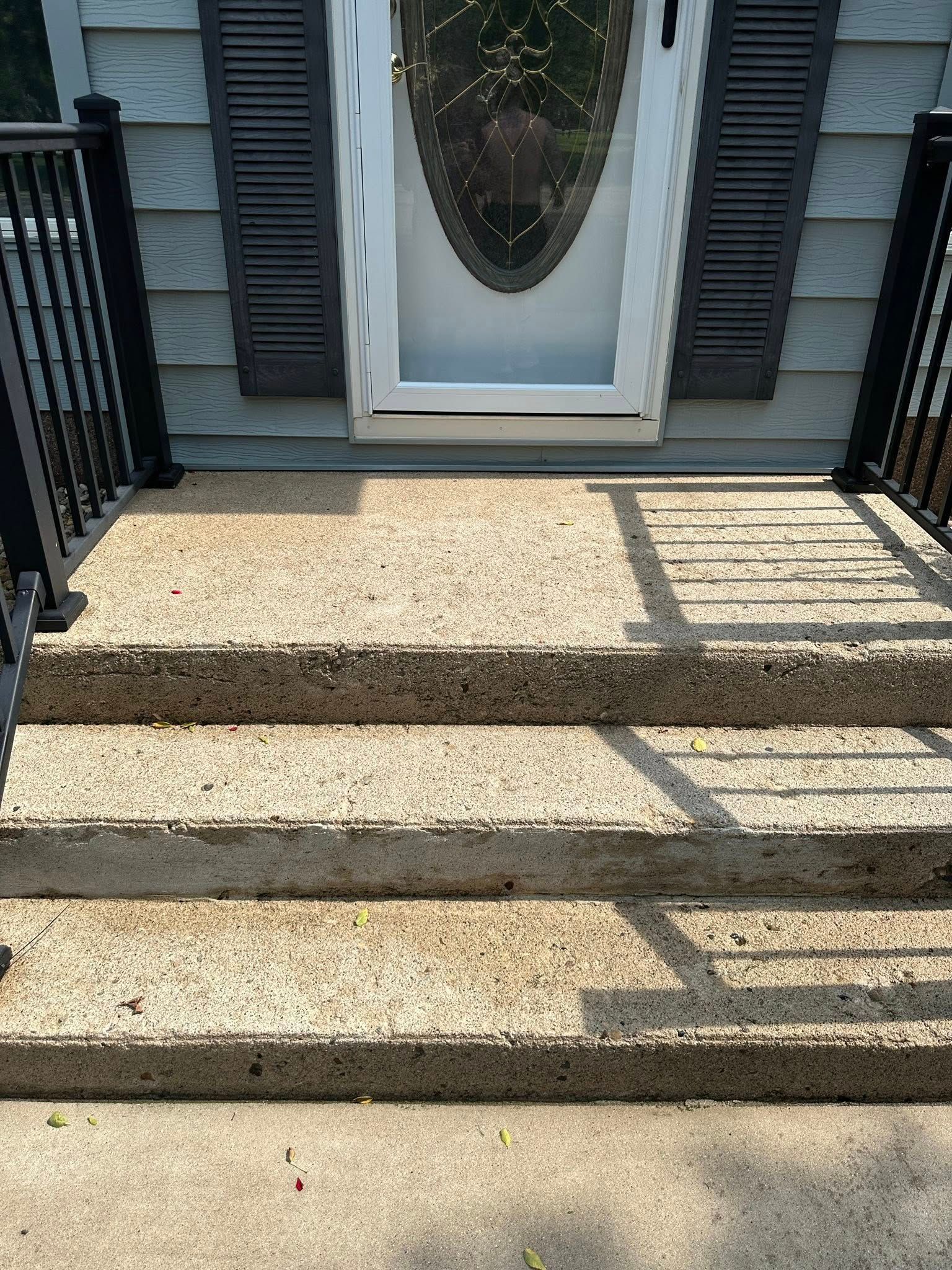 Three concrete steps leading up to a white door with an oval glass pane. Black shutters on either side.