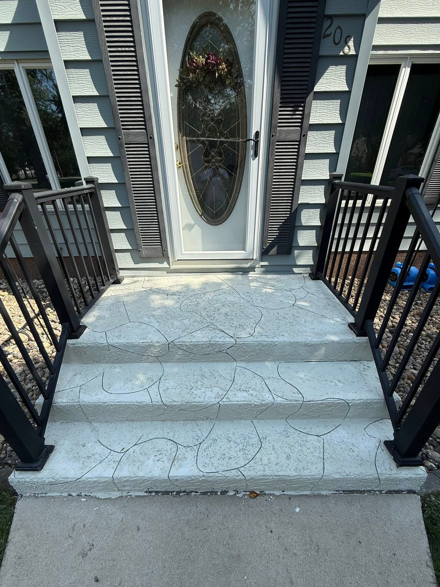 Concrete steps lead to a front door with a glass oval. Black railings flank the steps.