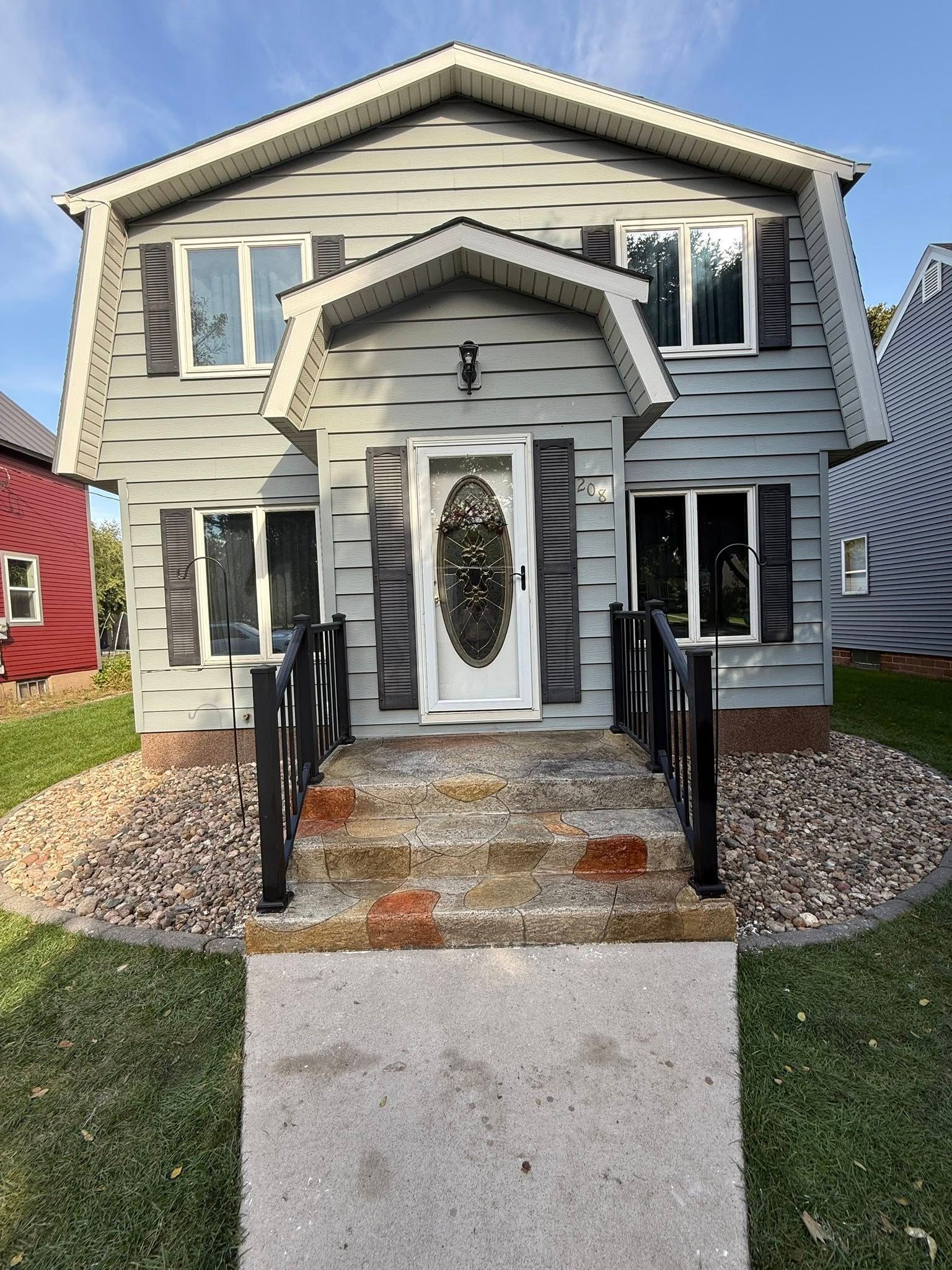Gray two-story house with black shutters, a white door, and a concrete walkway.