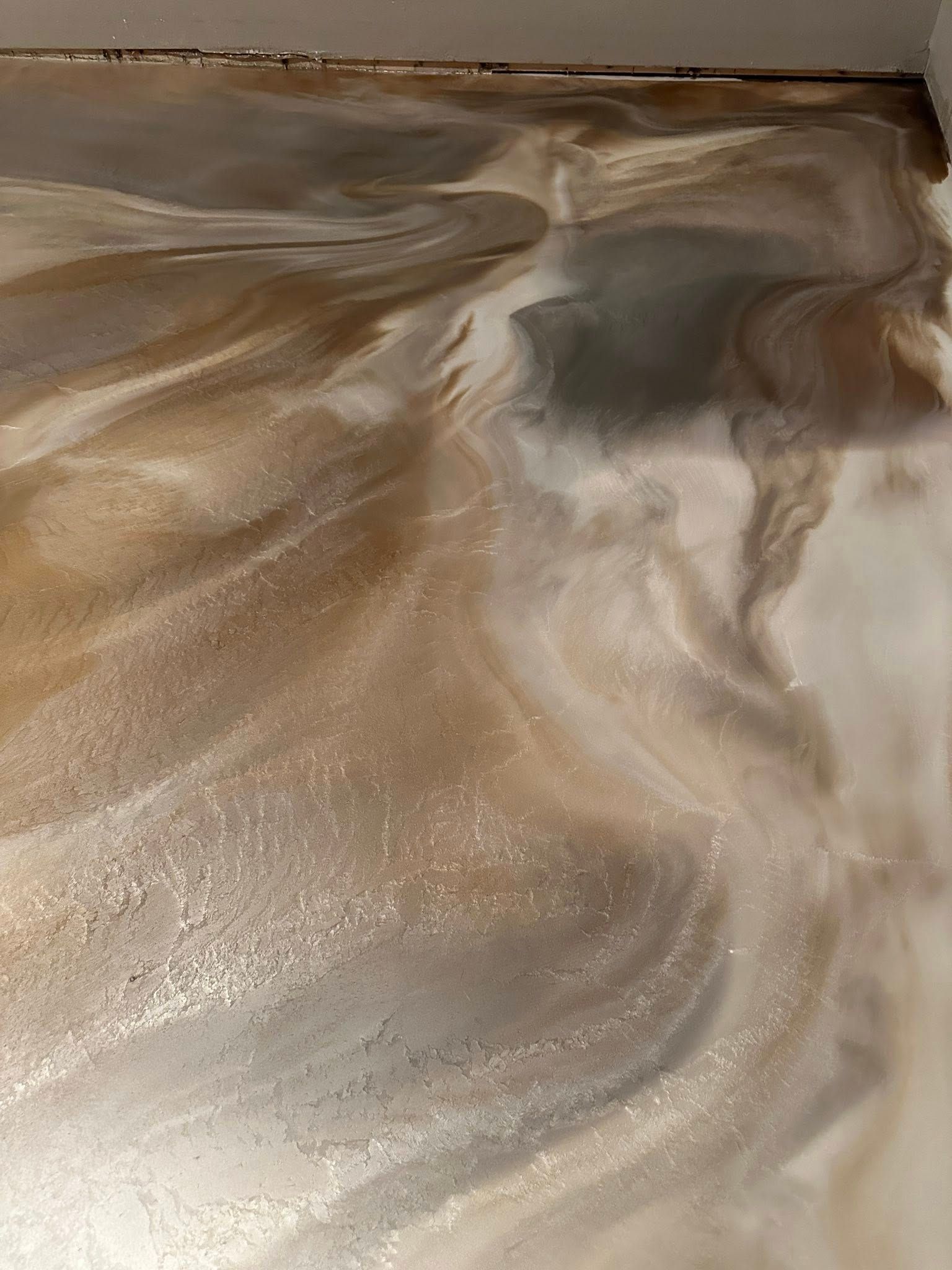 Swirling metallic epoxy floor in beige, gold, and silver tones.