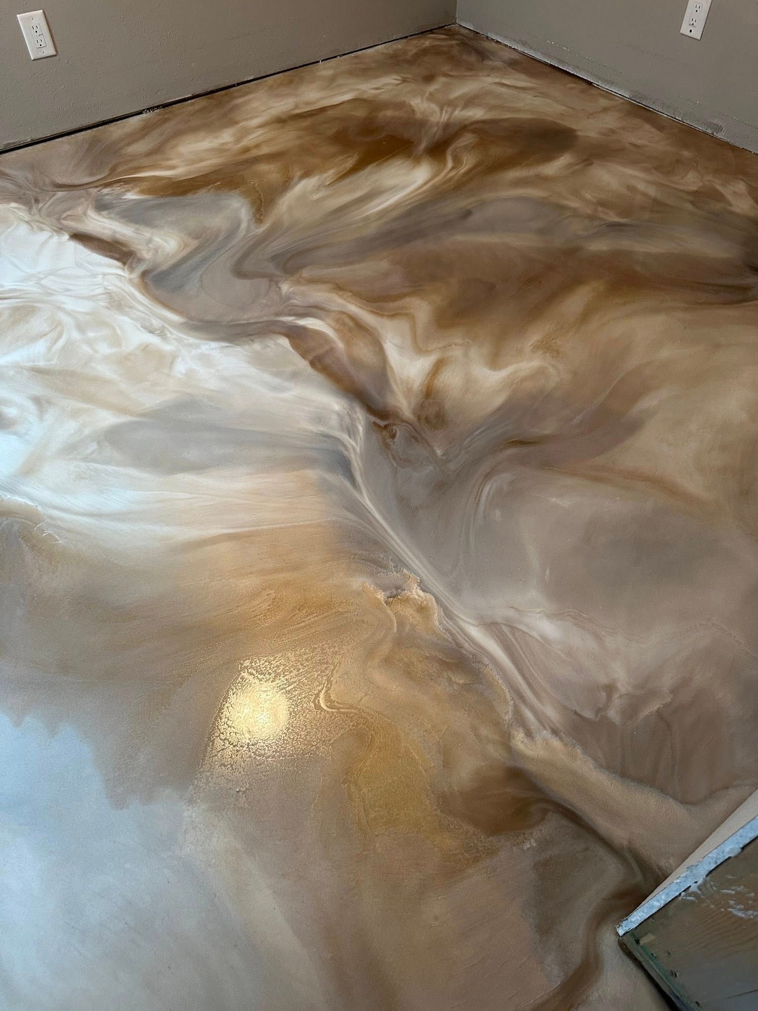 Metallic epoxy flooring with swirling gold, white, and brown patterns.