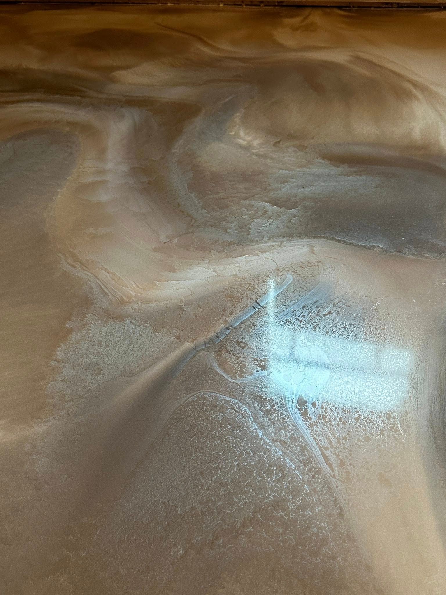 Swirled metallic epoxy floor with brown, silver, and white tones, reflecting a window's light.