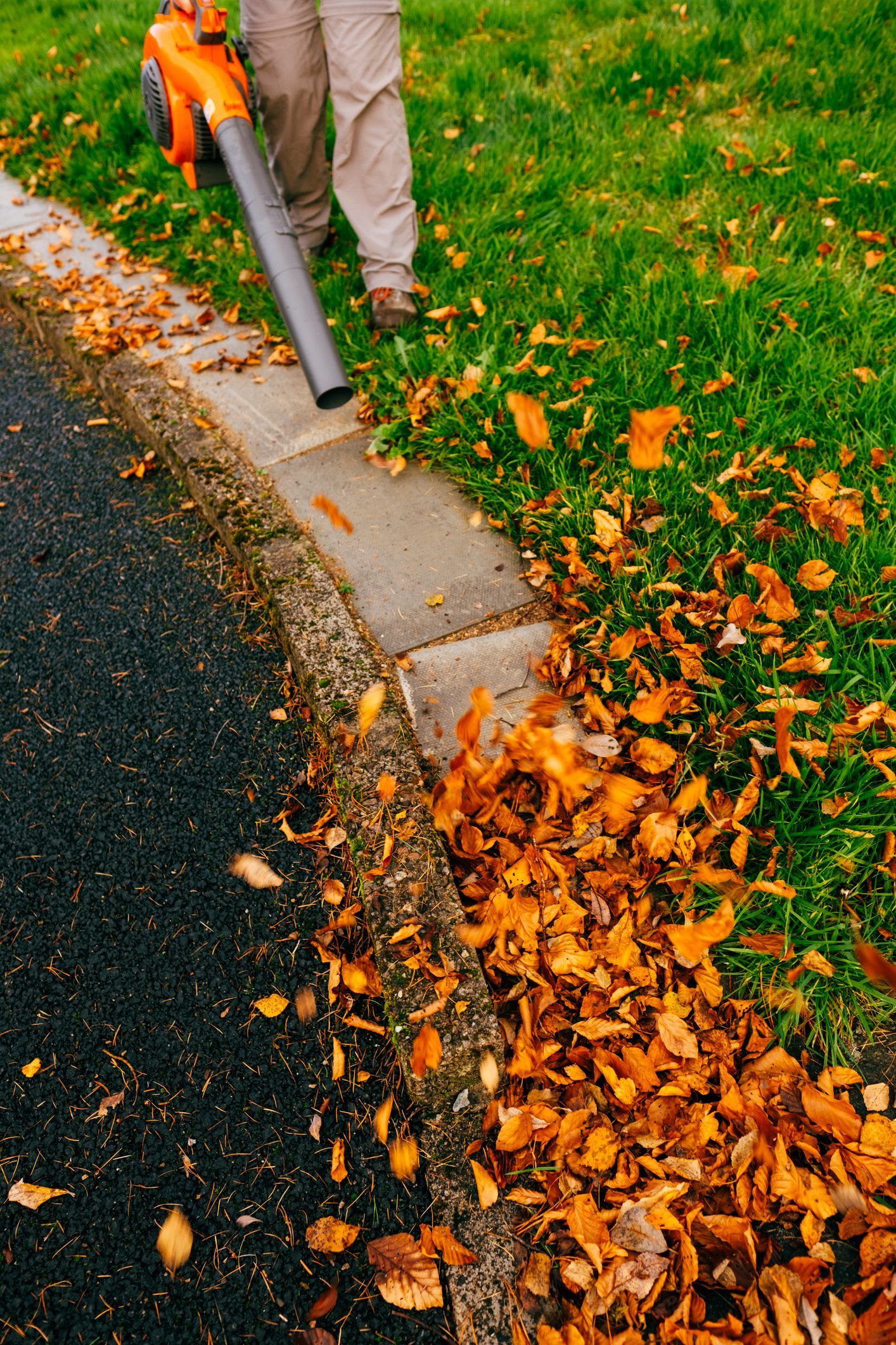 A person is blowing leaves off the side of the road.