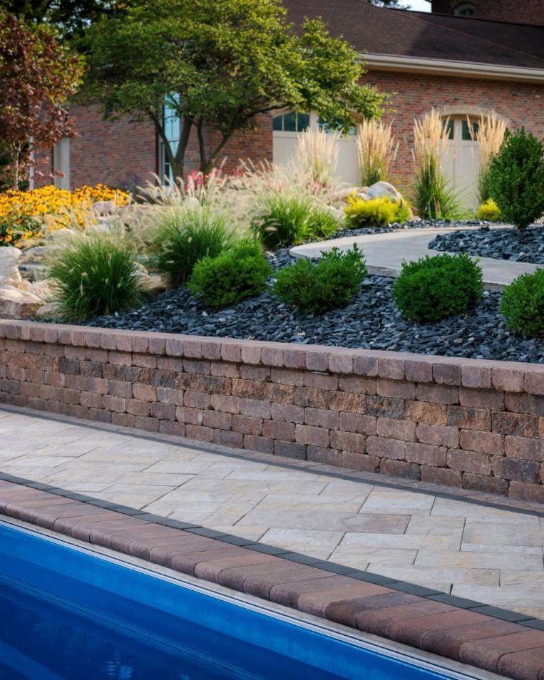 A brick wall surrounds a swimming pool with a house in the background