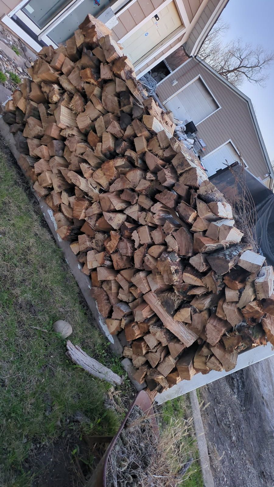 A pile of wood is sitting in front of a house.