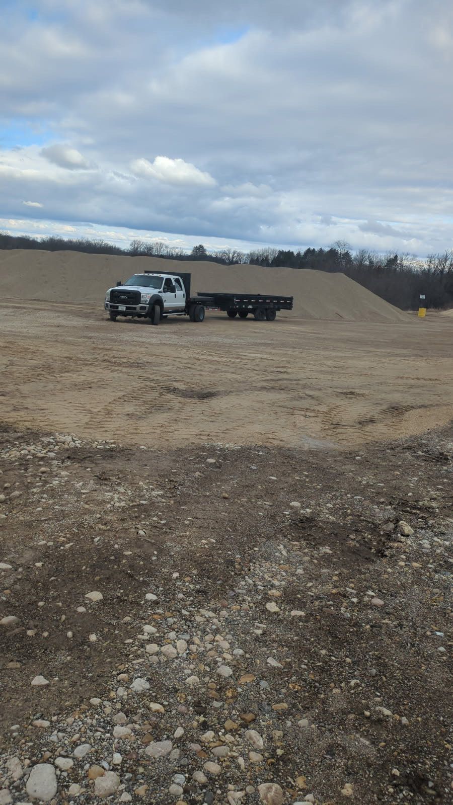 A truck with a flatbed trailer is parked in a dirt field.