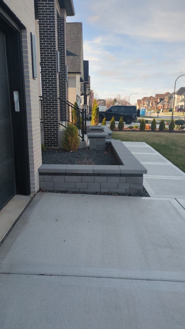 A concrete walkway leading to a house with a black garage door.
